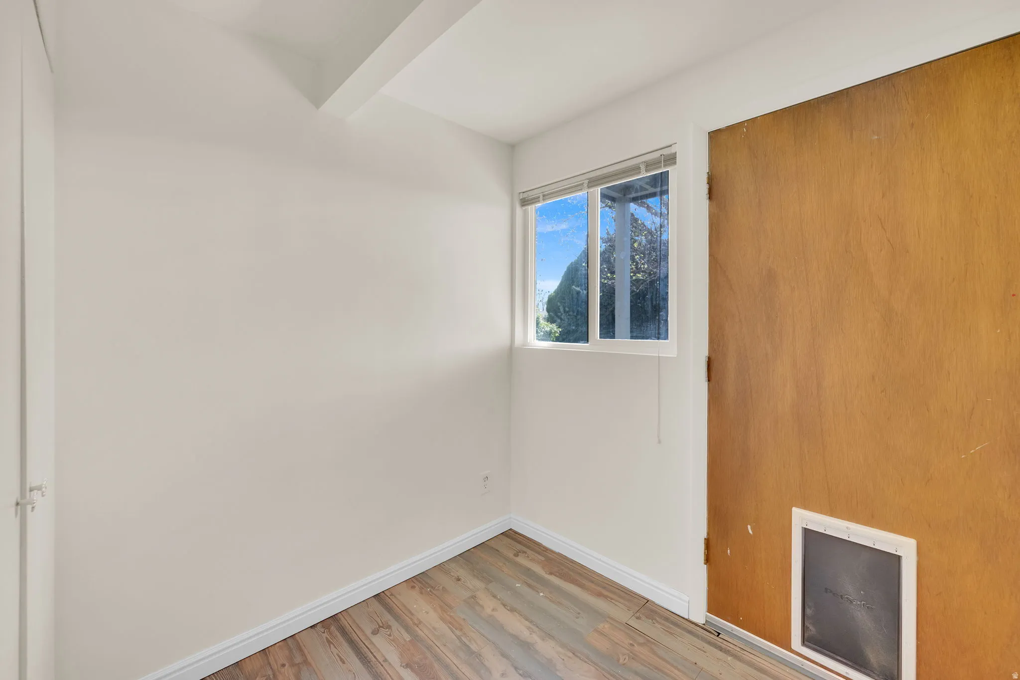 Room with wood-finish flooring, white walls, and a window providing natural illumination
