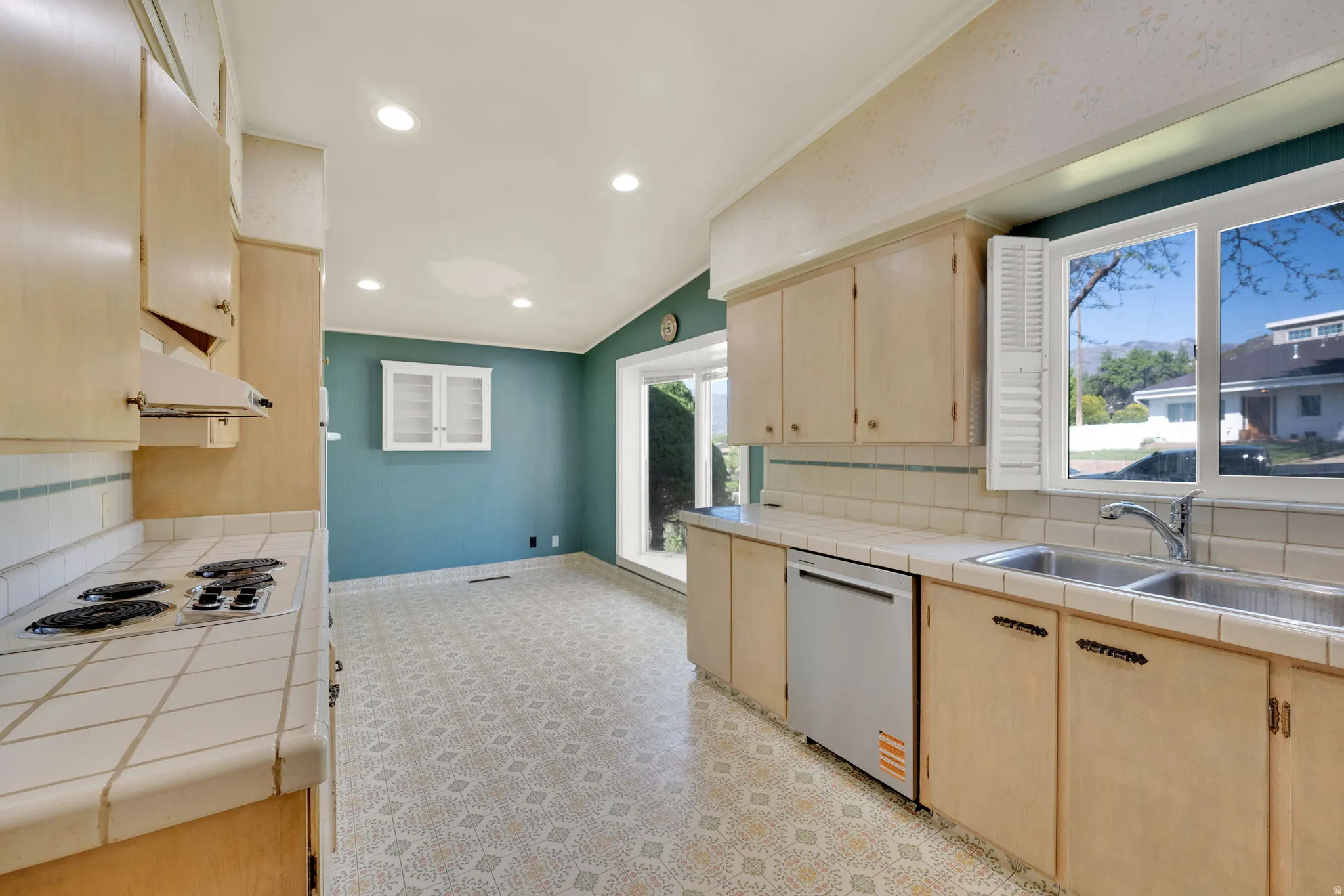 Kitchen featuring light-toned cabinetry, tile countertops, a double basin sink, and a built-in dishwasher