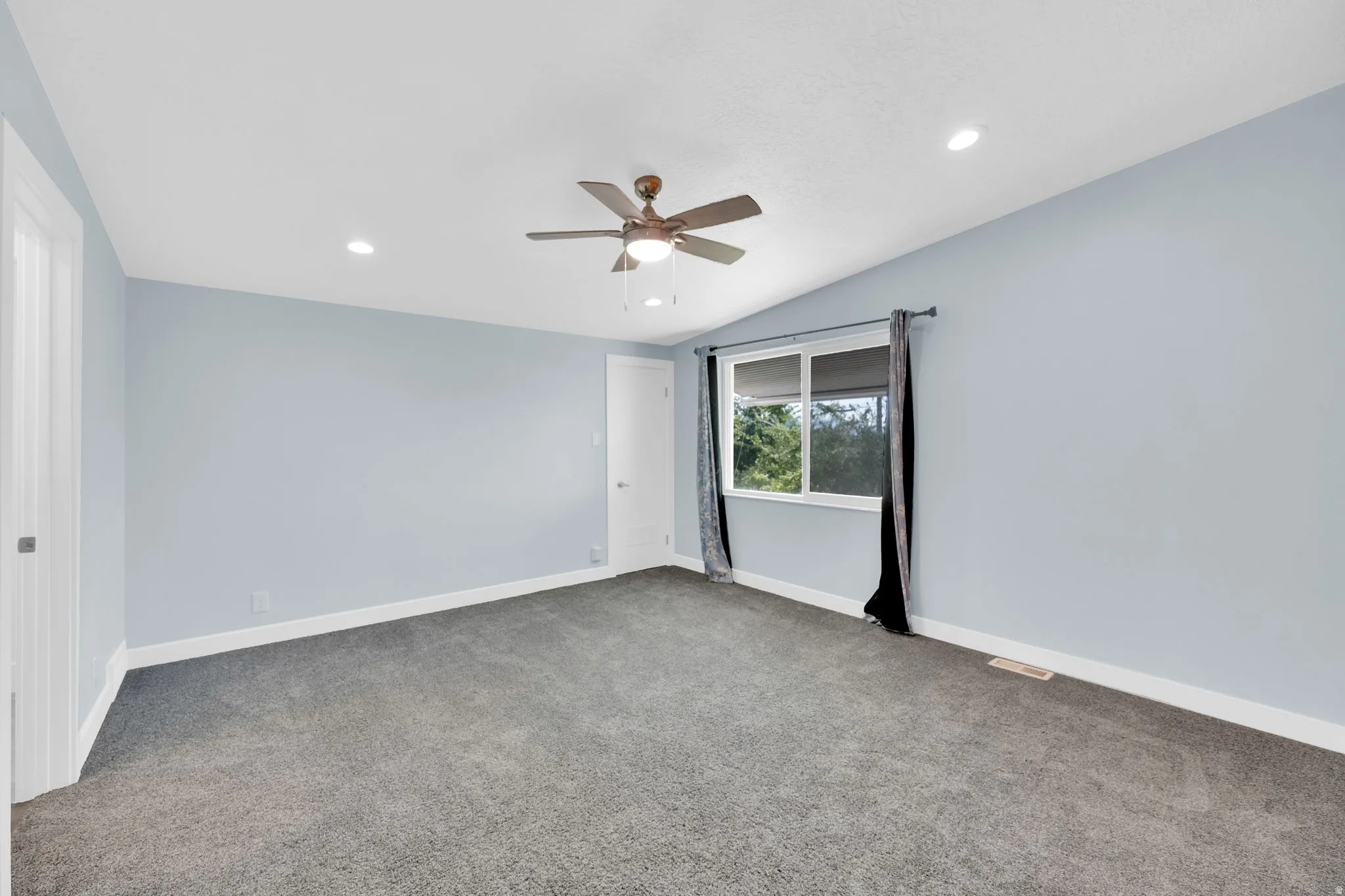 Spacious room featuring light blue walls, gray carpet, and a white trim baseboard