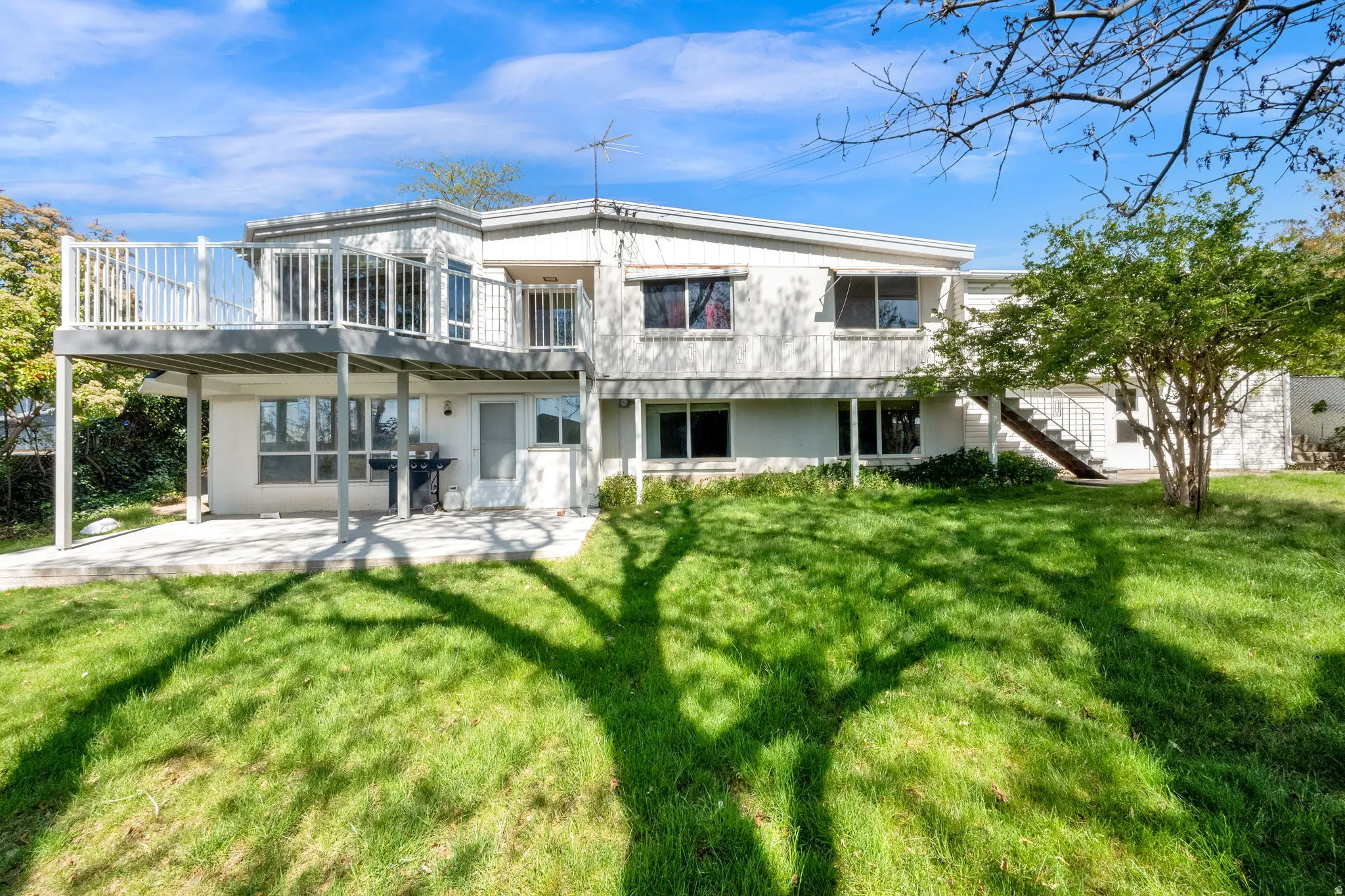 Multi-level residence featuring a large upper-level deck with white railings, a lower-level patio, and a spacious green lawn