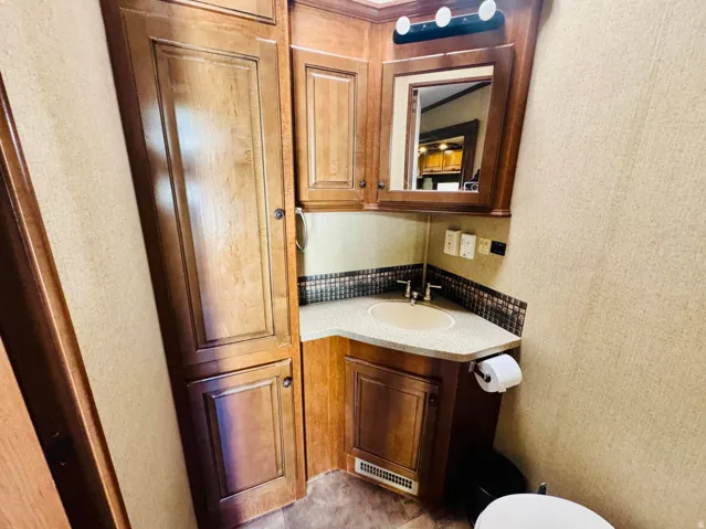 Corner vanity with integrated sink, mosaic tile backsplash, and overhead mirrored cabinetry