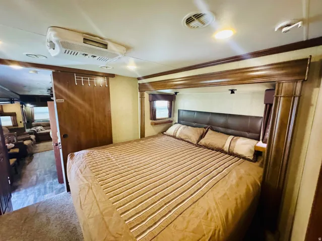 Bedroom area featuring a leather-look headboard, integrated shelving, wood-finish trim, recessed lighting, and an overhead air conditioning unit