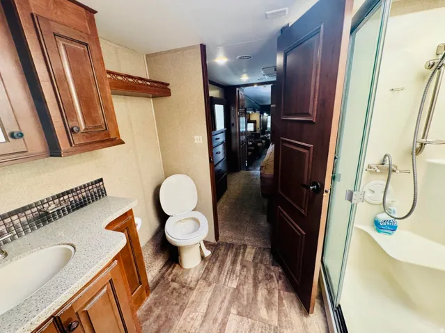 Bathroom featuring a shower enclosure with a glass door, a toilet, a vanity with an integrated sink, a mosaic tile backsplash, and wood-finish flooring