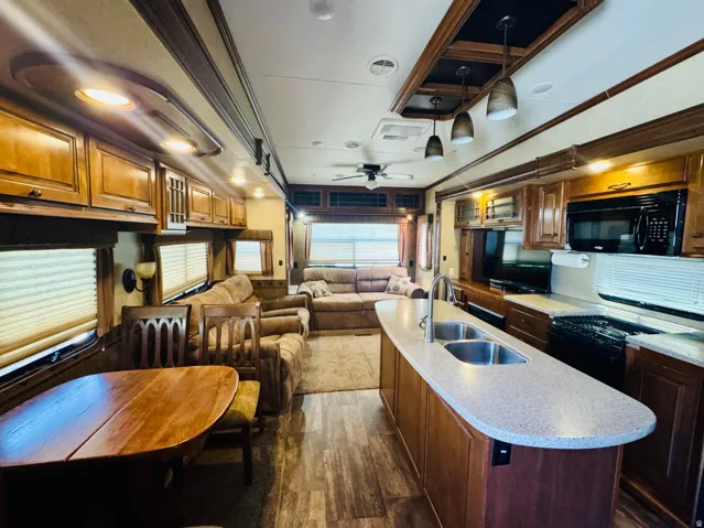 Open-concept living space featuring wood-finish flooring, a kitchen island with dual sinks and stone-finish countertop, dark wood cabinetry, a built-in microwave, and recessed lighting