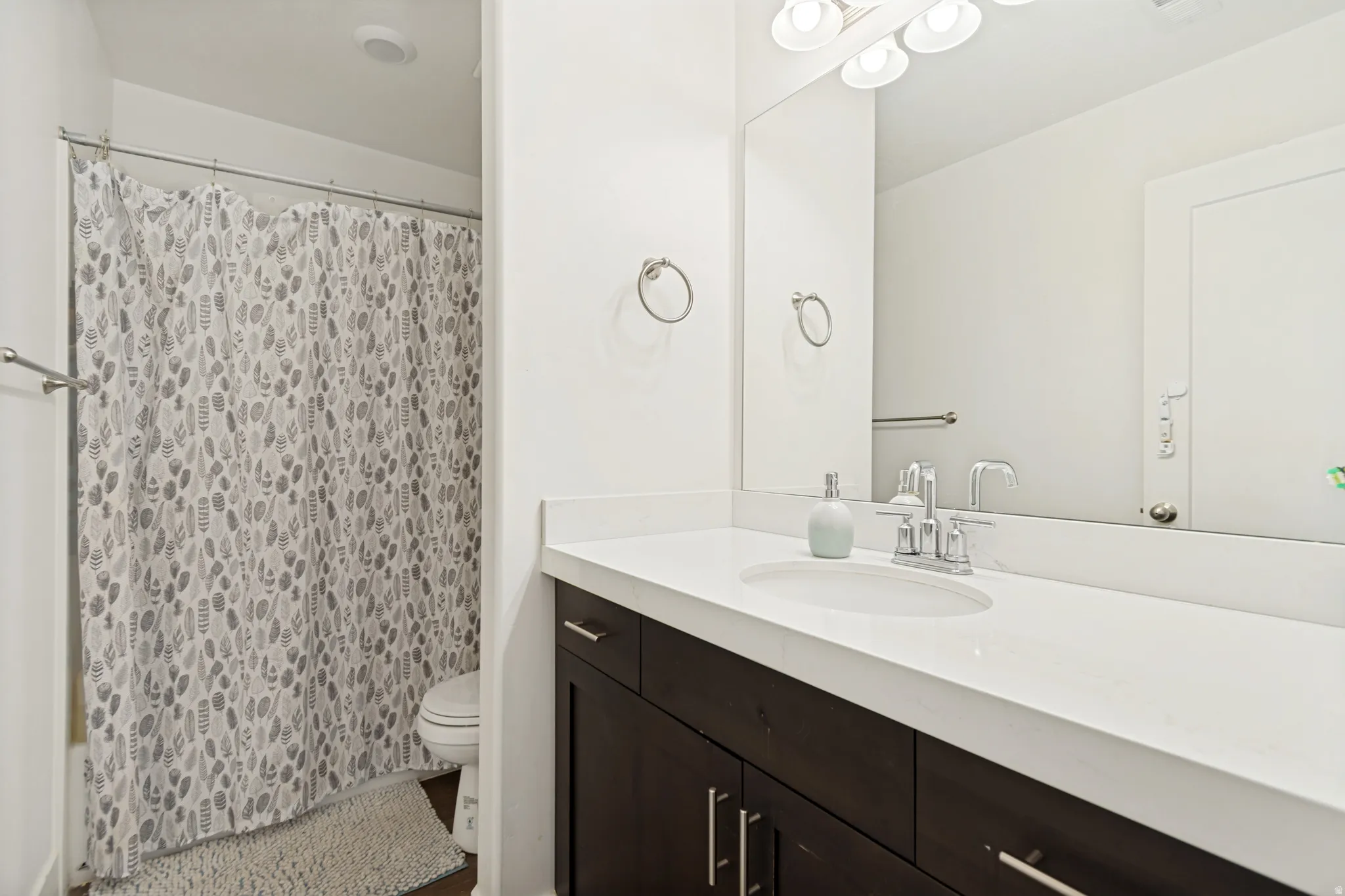 Bathroom featuring a dark wood-finish vanity with an integrated sink, polished chrome faucet, and a large wall-mounted mirror