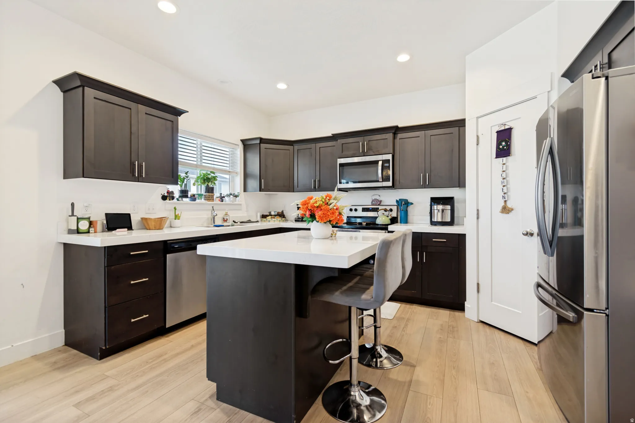 Kitchen featuring dark wood cabinetry, light-toned countertops, stainless steel appliances, and wood-finish flooring