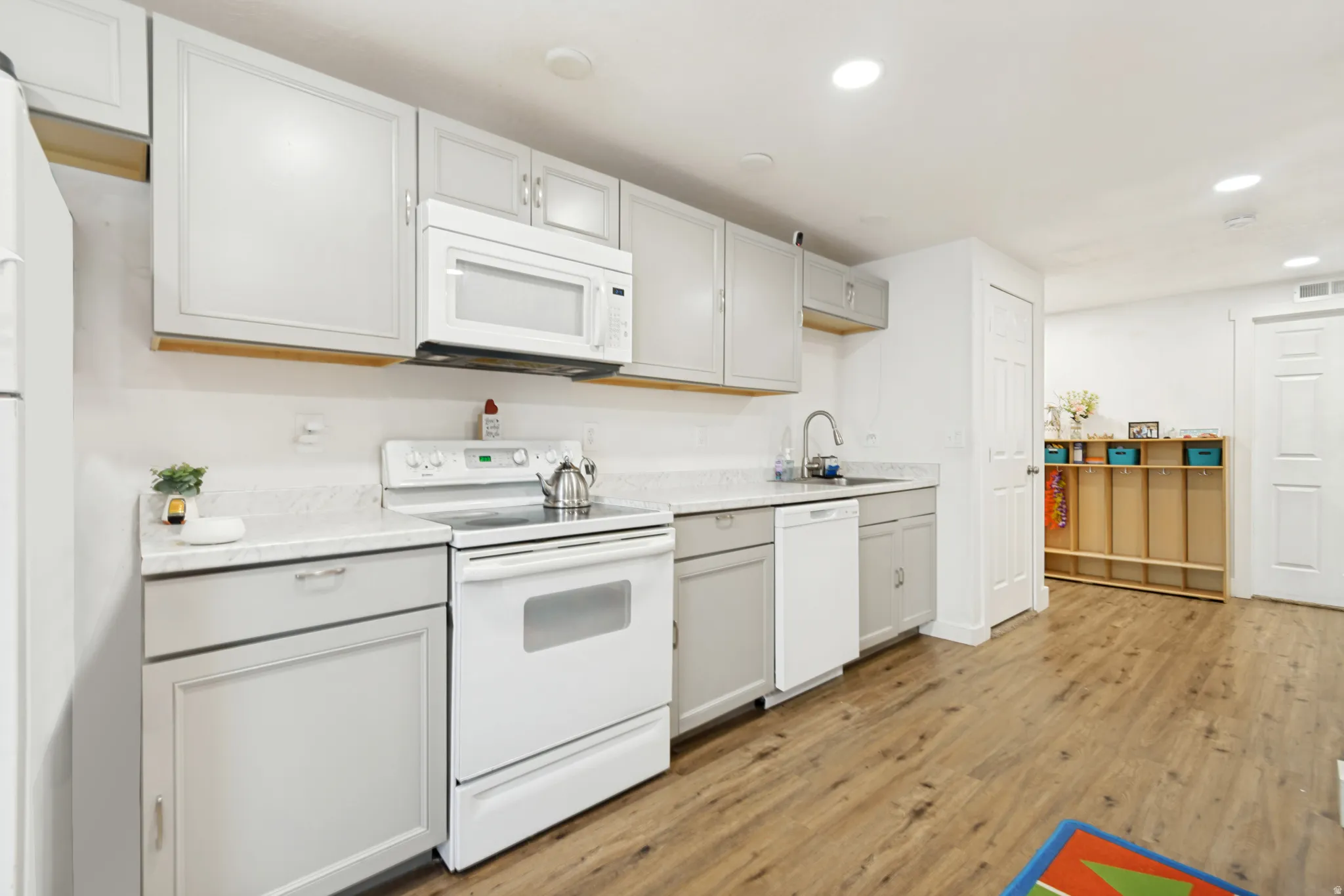 Kitchen featuring light gray cabinetry, white appliances, durable wood-finish flooring, recessed lighting, and a neutral countertop