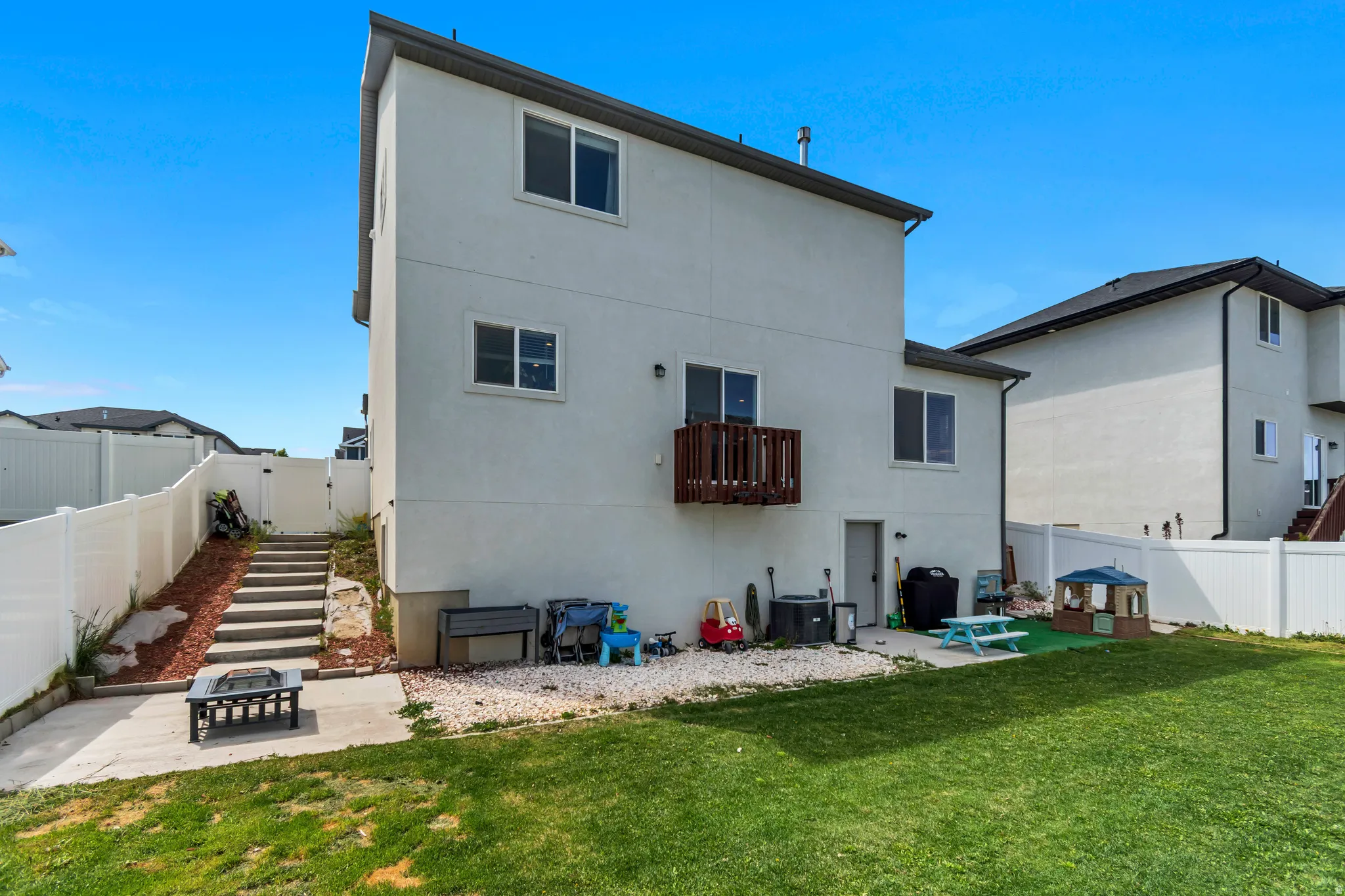 Spacious backyard featuring a manicured lawn, white privacy fencing, and a concrete patio with a built-in fire pit