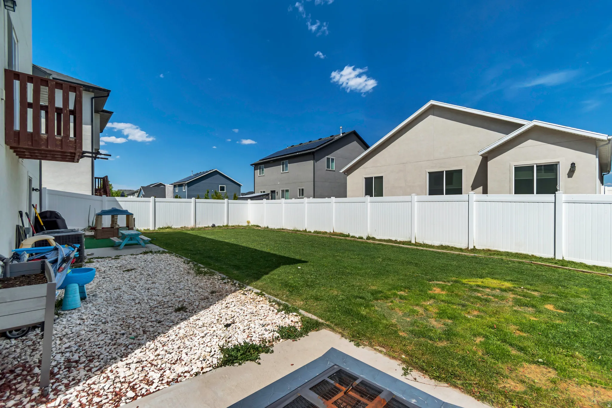 Expansive backyard featuring a white vinyl fence, gravel landscaping, and a manicured lawn