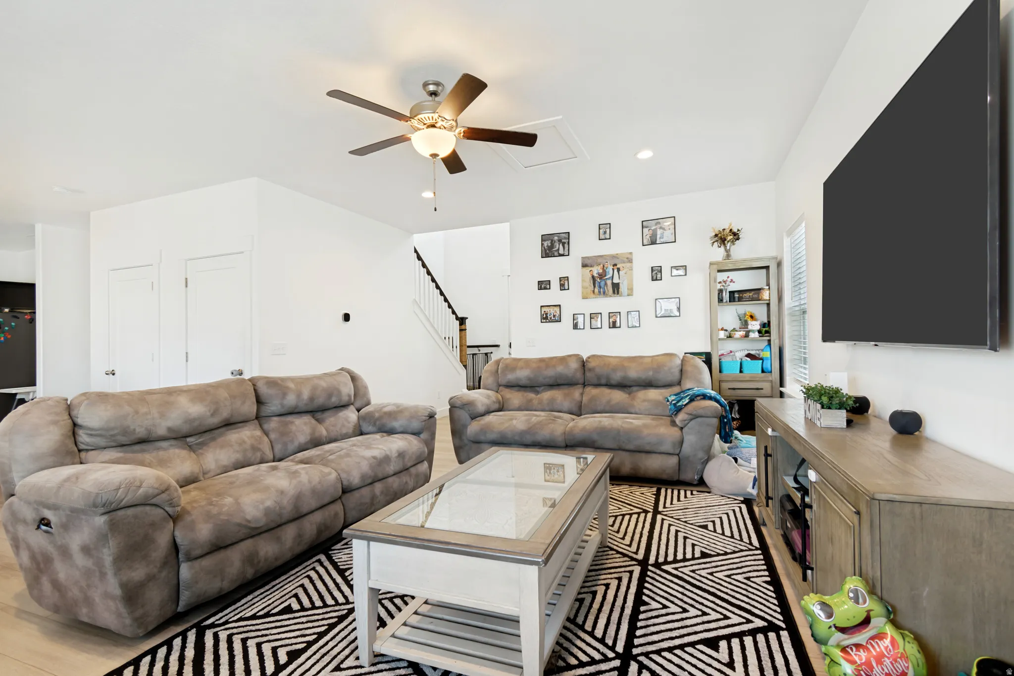 Open-concept living area featuring light wood-finish flooring, a ceiling fan with integrated lighting, and multiple recessed lights