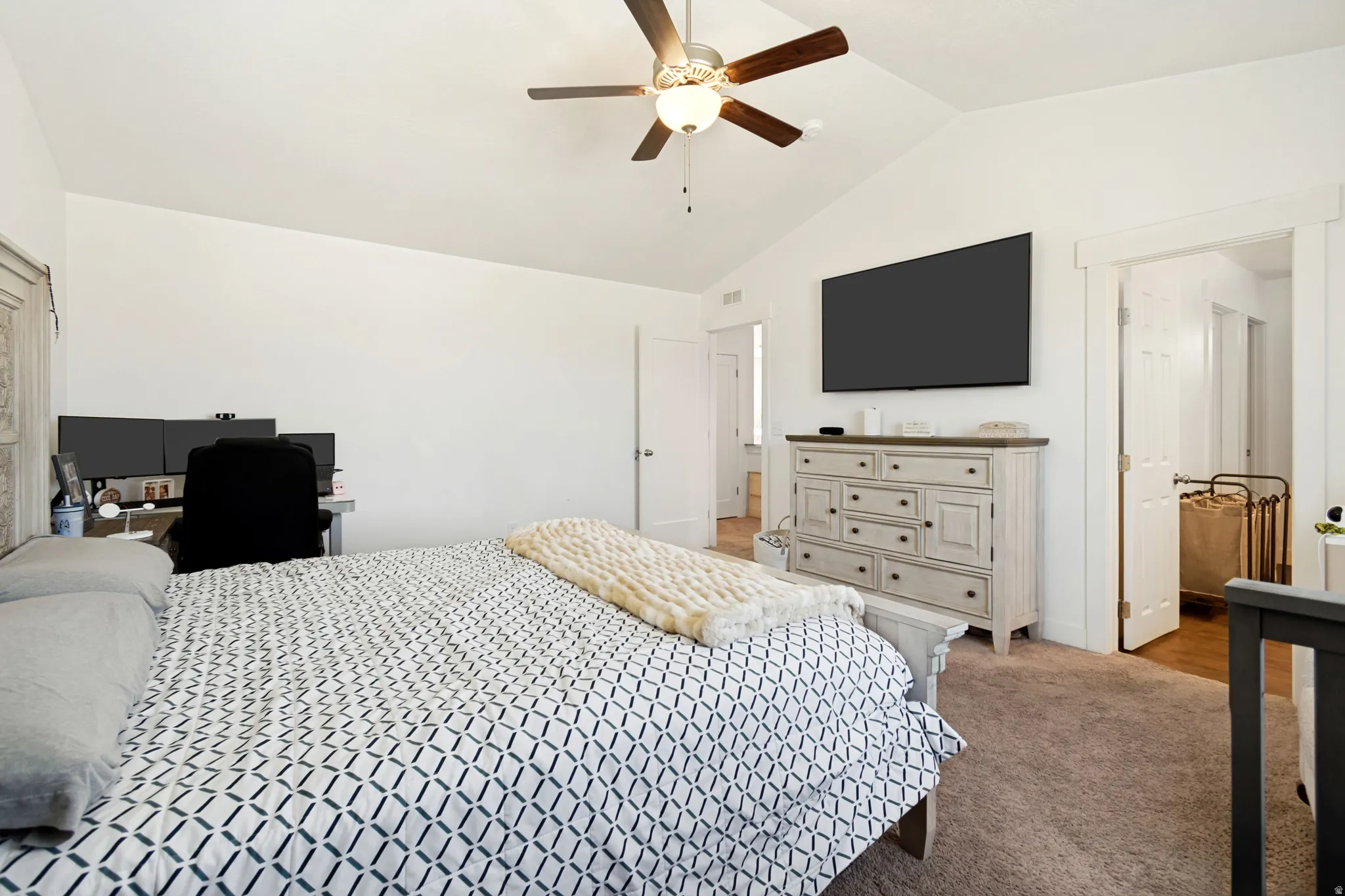 Vaulted ceiling bedroom featuring a ceiling fan, wall-mounted television, and carpeted flooring
