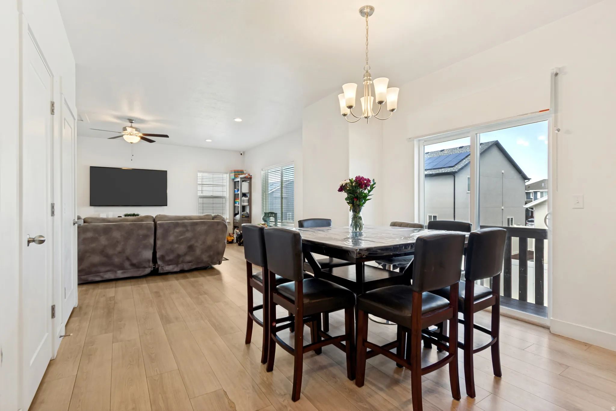 Open-concept dining area featuring wood-finish flooring, a contemporary chandelier, and direct access to a balcony through sliding glass doors