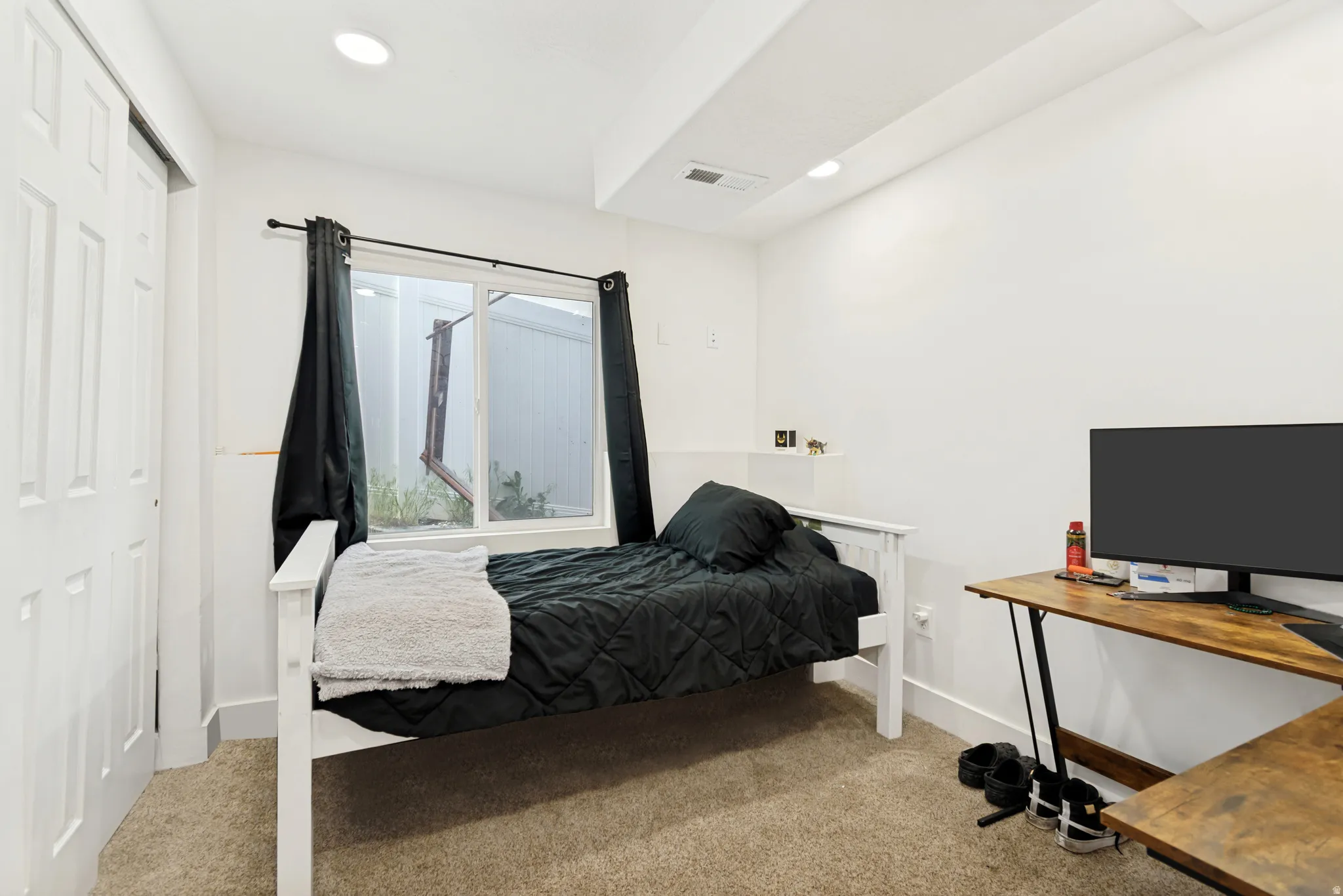 Carpeted room featuring a white sliding closet door, recessed lighting, and a window with black privacy curtains