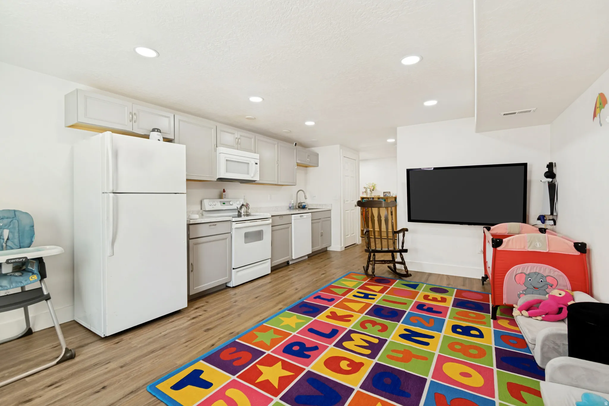 Open-concept lower level featuring recessed lighting, wood-finish flooring, and a full kitchen with white appliances and light gray cabinetry