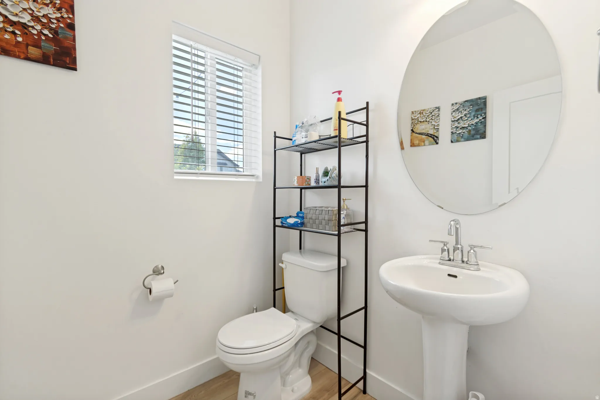Pedestal sink with chrome faucet, circular wall mirror, and light wood-finish flooring