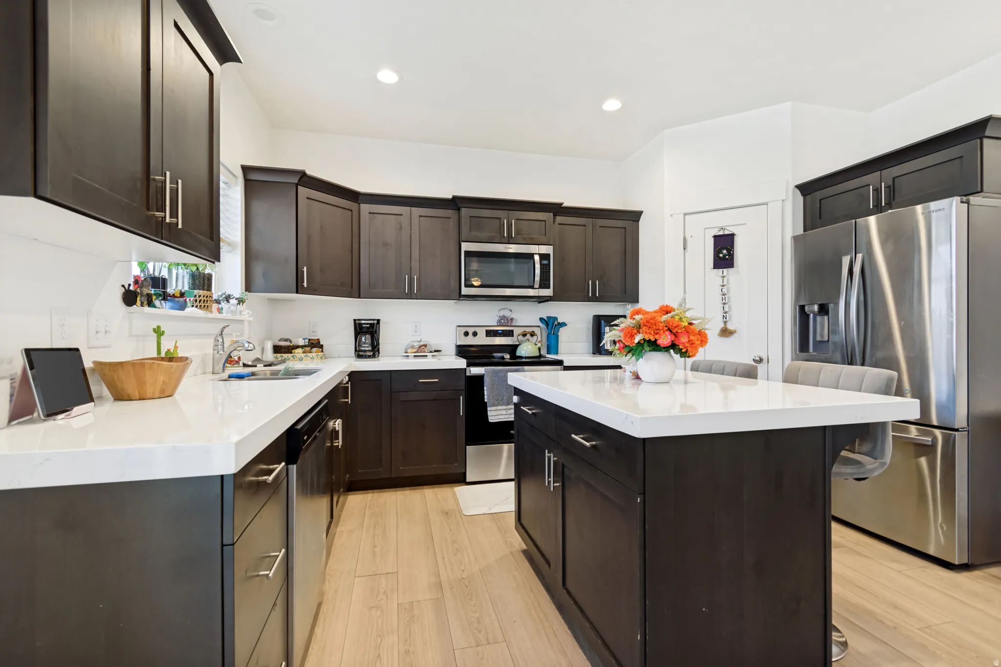 Modern kitchen featuring dark wood cabinetry, light wood-finish flooring, recessed lighting, white countertops, and a stainless steel appliance package