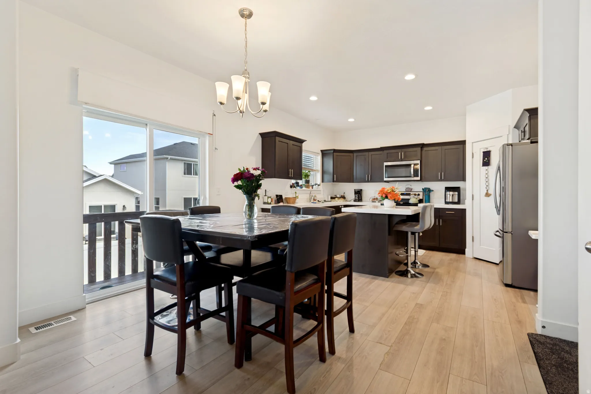 Spacious kitchen and dining area featuring light wood-finish flooring, dark wood cabinetry, a center island with a light-toned countertop, and stainless steel appliances