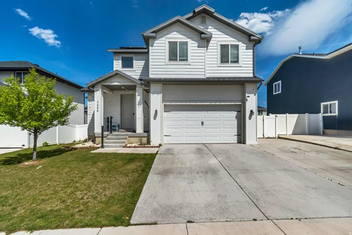 Two-story residence featuring light-colored siding, an attached two-car garage, a covered front porch, and a concrete driveway