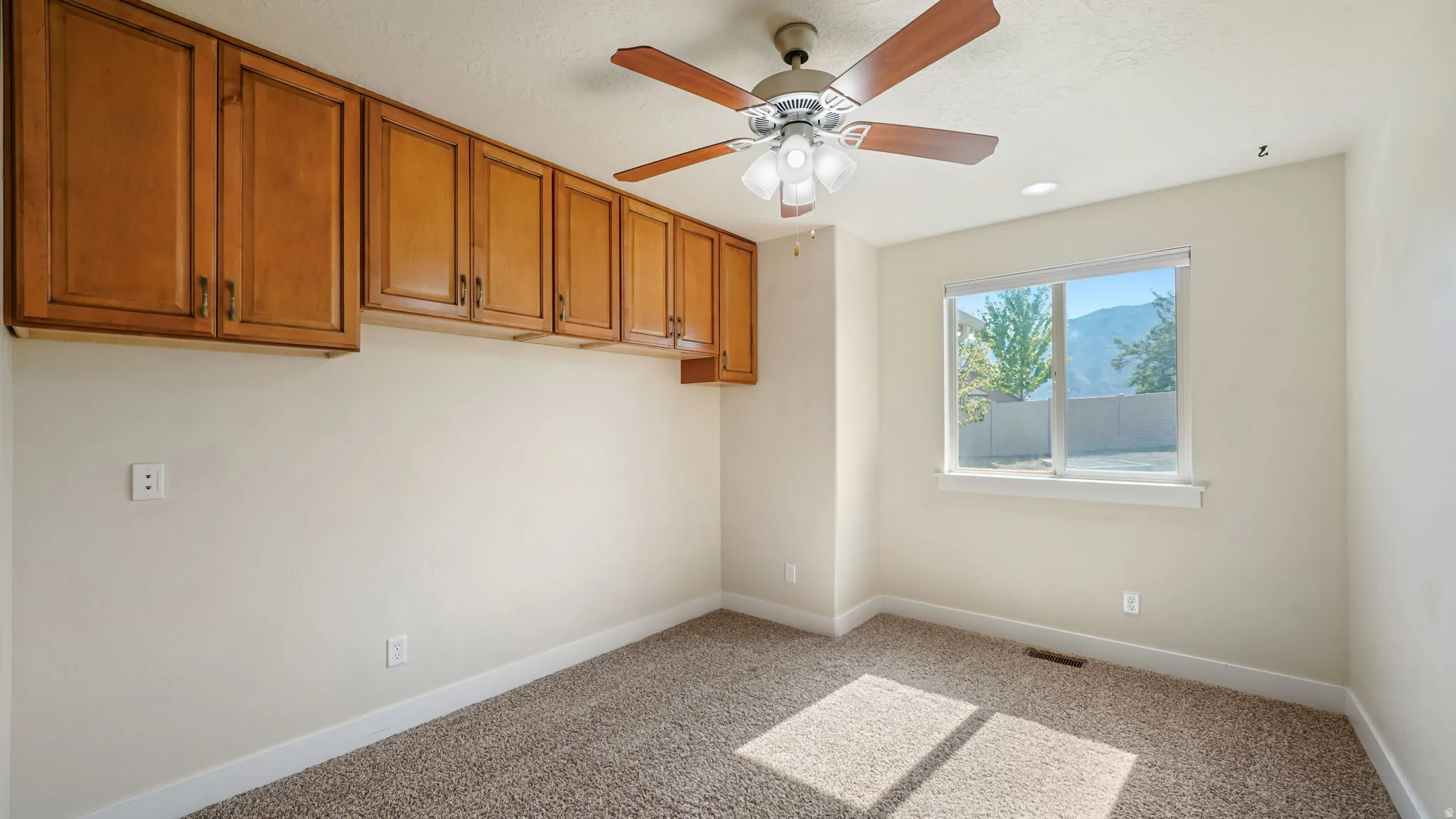 Room featuring extensive wood cabinetry, ceiling fan with integrated lighting, and a window with mountain scenery
