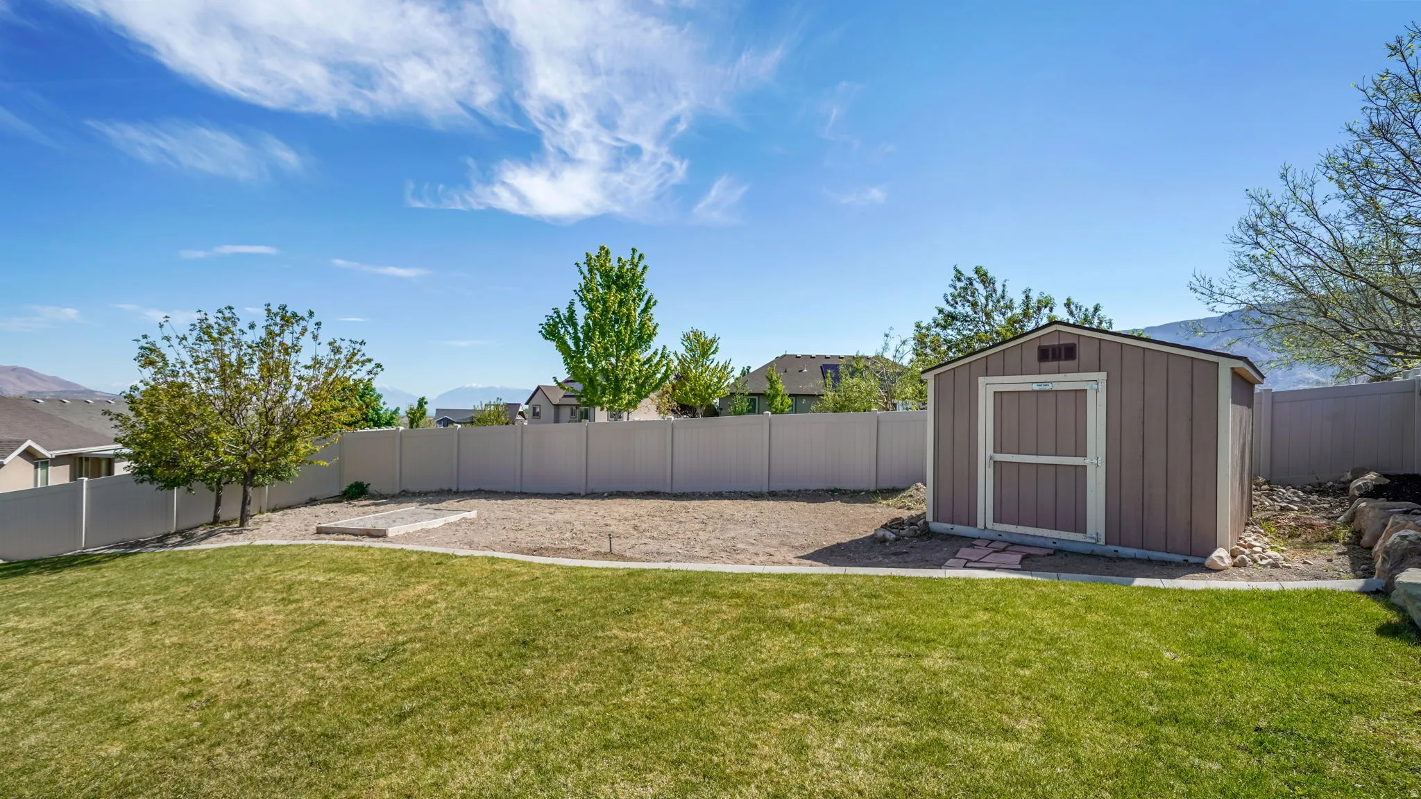 Expansive backyard featuring a manicured lawn, a gravel area, a private fence, and a storage shed