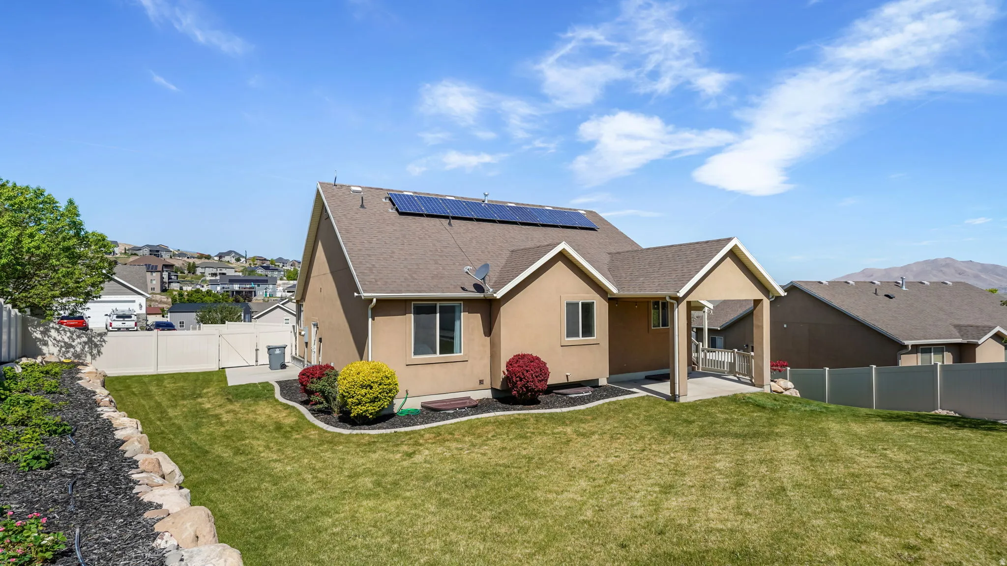 Rear exterior featuring a covered patio, solar panels, and a fenced yard with established landscaping