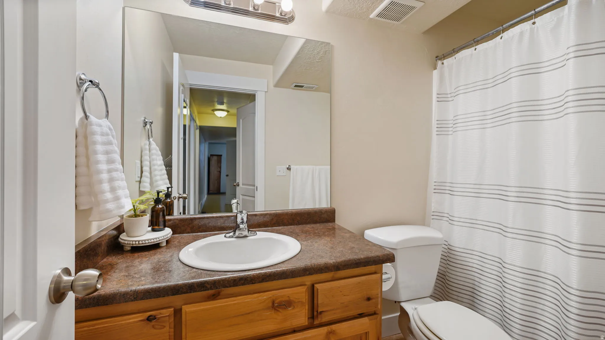 Bathroom featuring a wood-finish vanity with a built-in sink, a large mirror, and overhead lighting