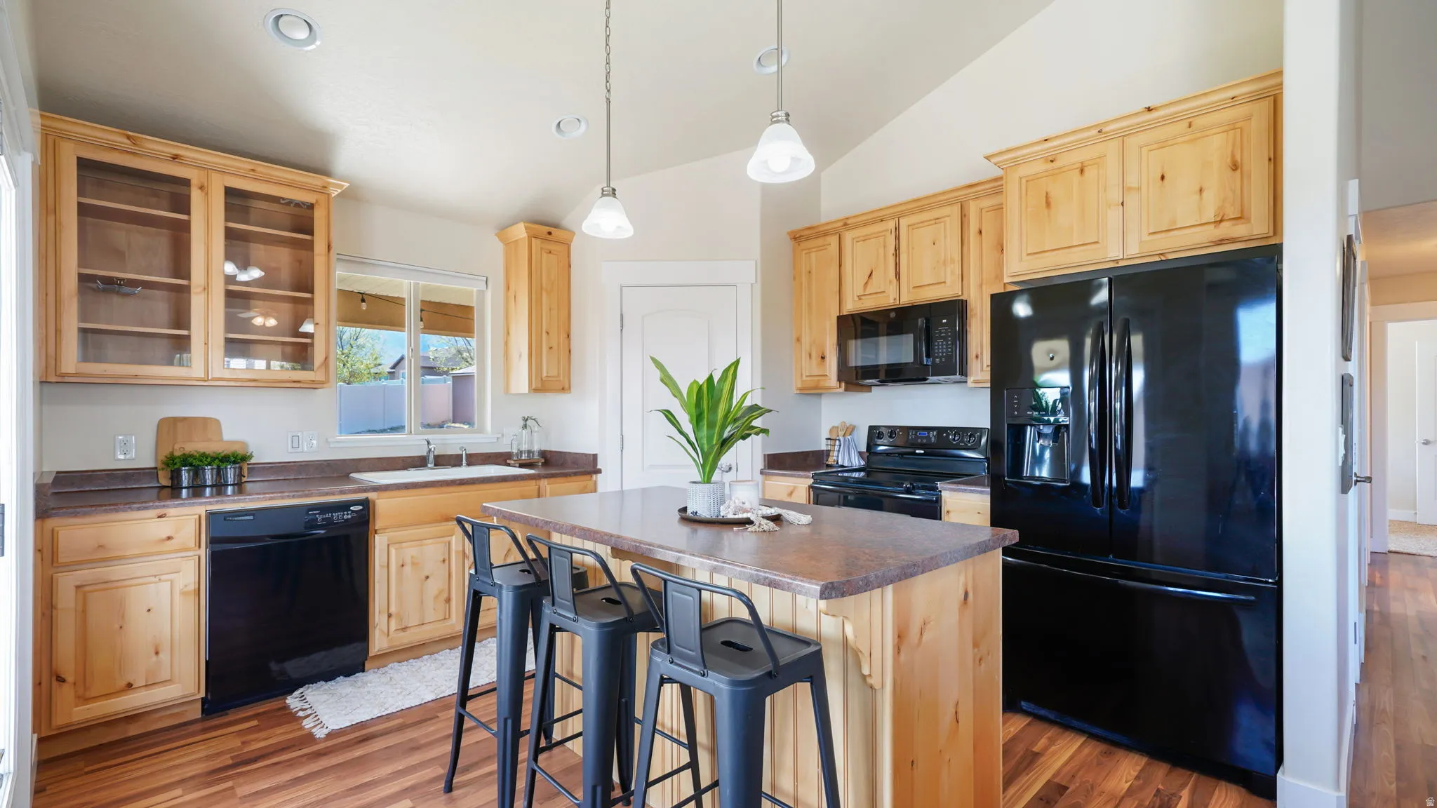 Kitchen featuring wood-finish cabinetry, black appliances, a central island with seating, a window above the sink, and wood-finish flooring