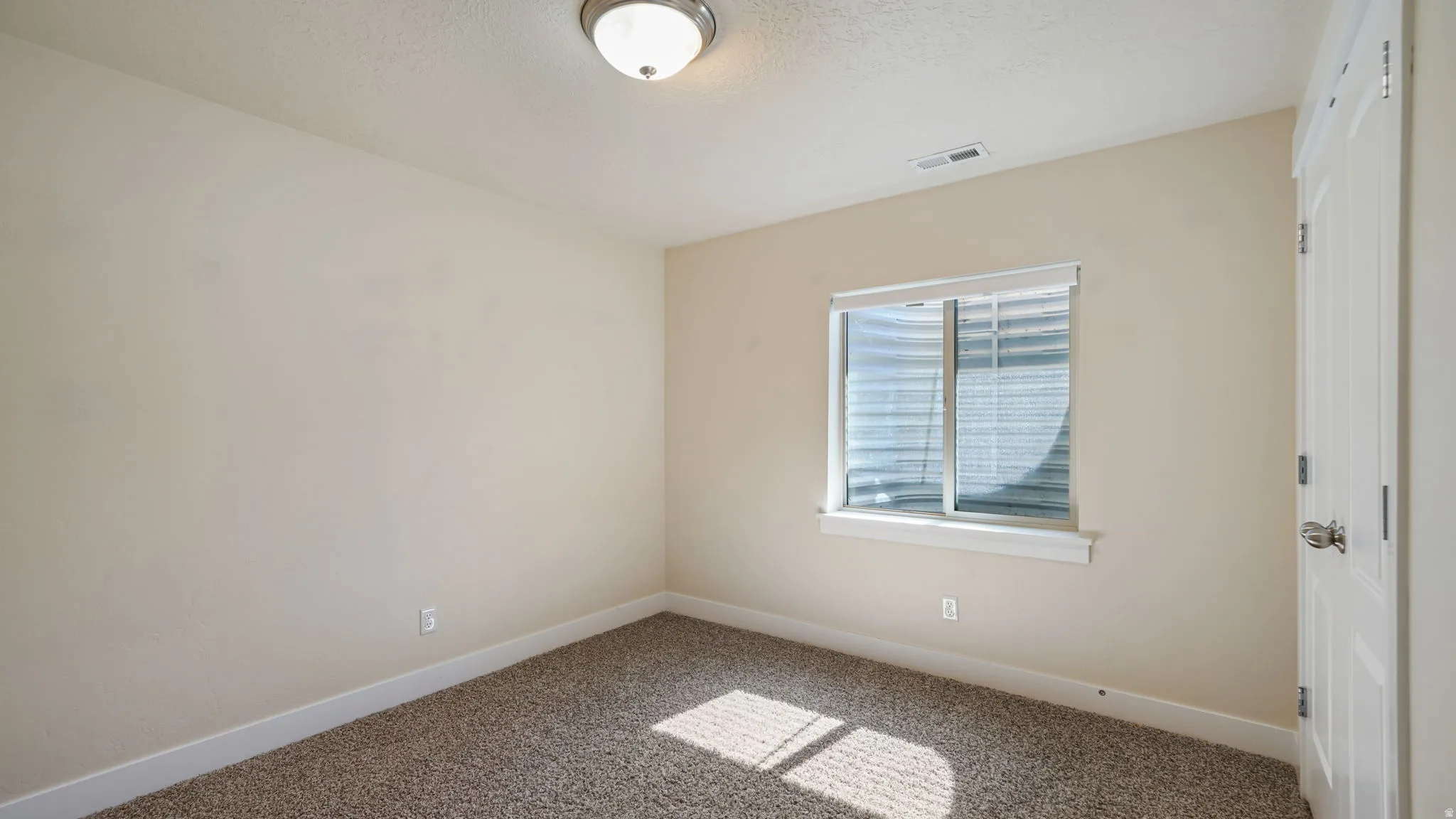 Neutral toned walls with a contrasting white trim and a textured carpeted floor create a versatile interior space