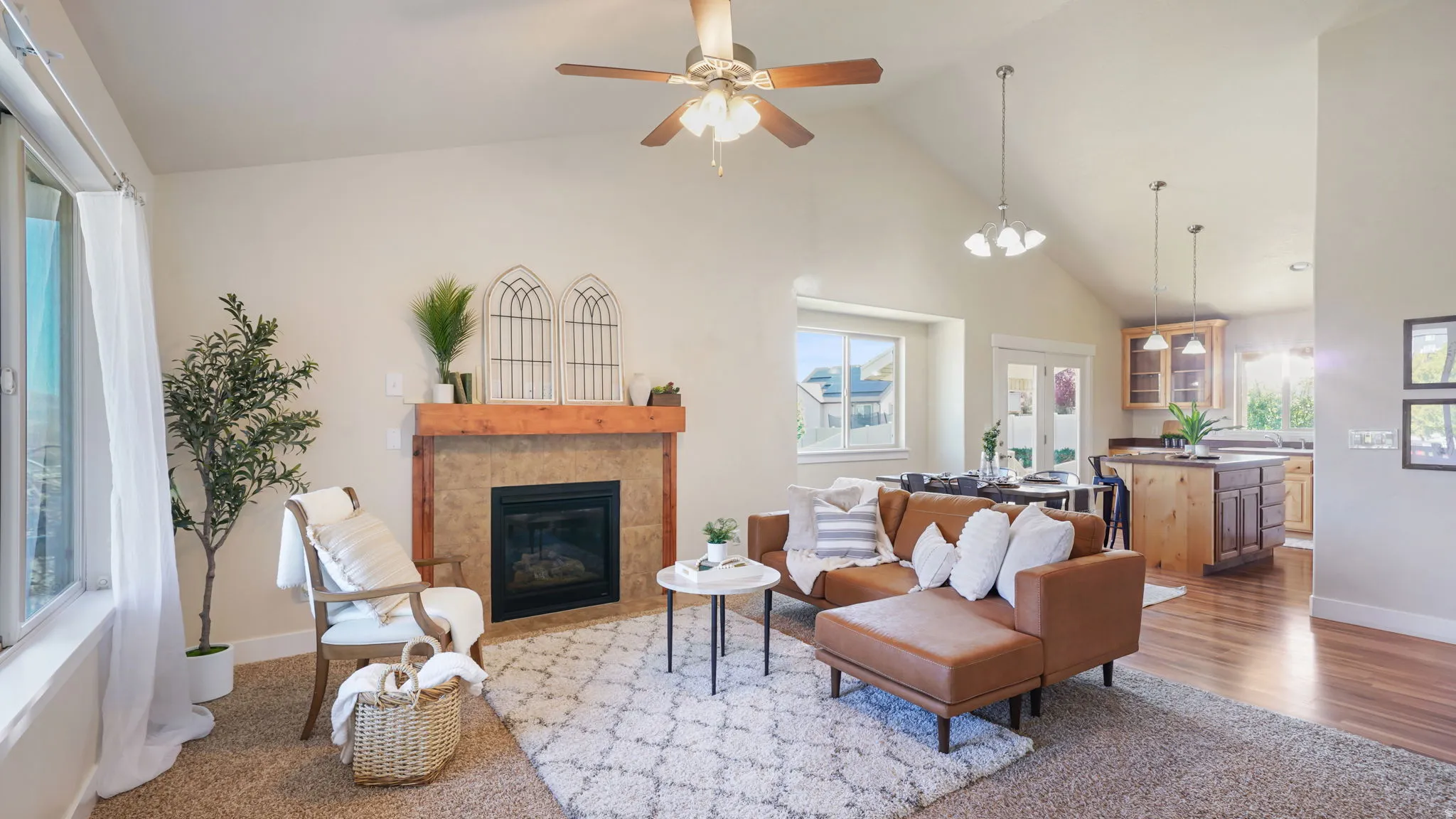 Vaulted ceiling living area featuring a fireplace with a wood mantle and stone-look surround, a ceiling fan, and large windows