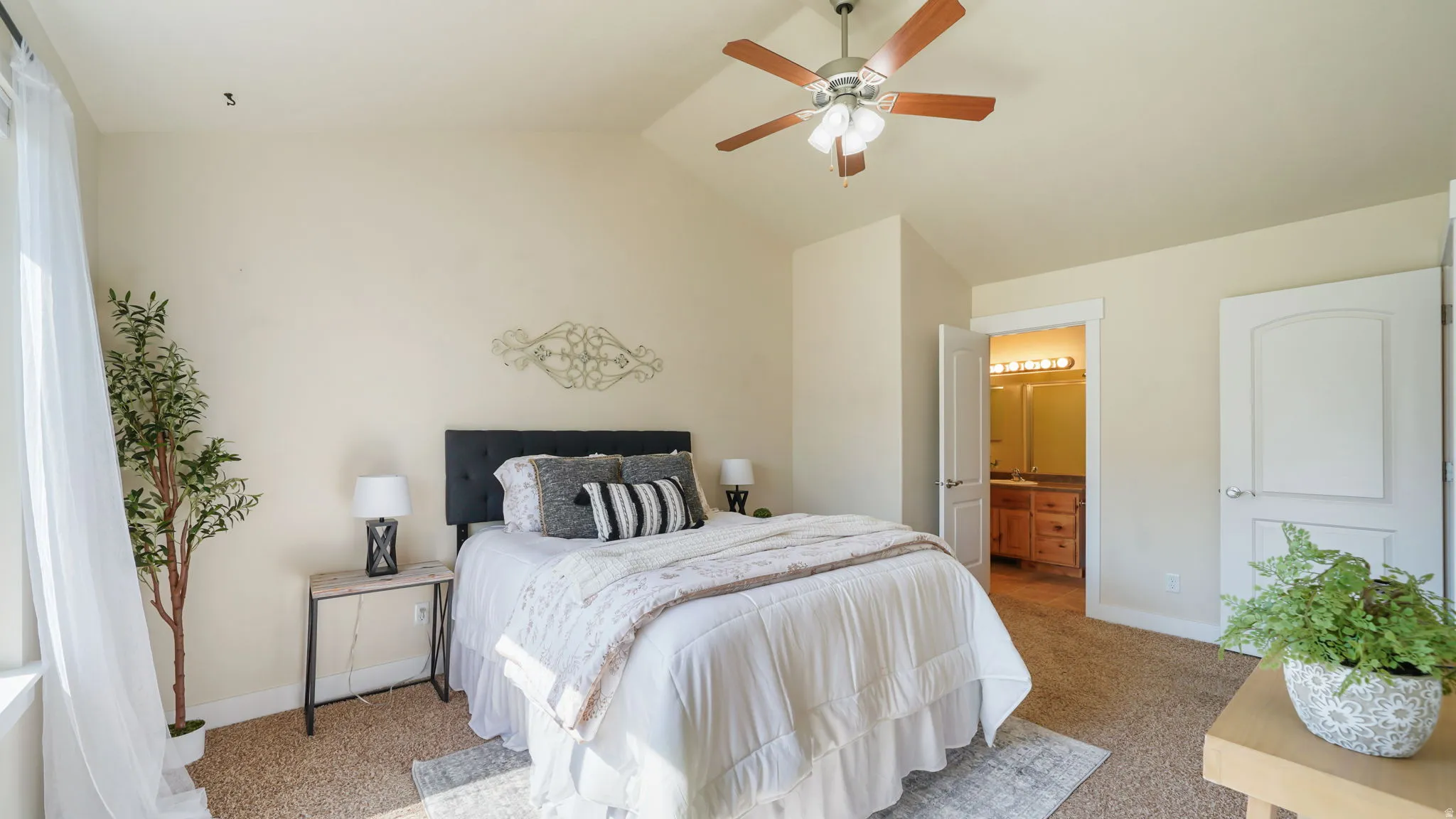 Carpeted bedroom featuring a ceiling fan with integrated lighting, a tall window with sheer curtains, and a solid interior door