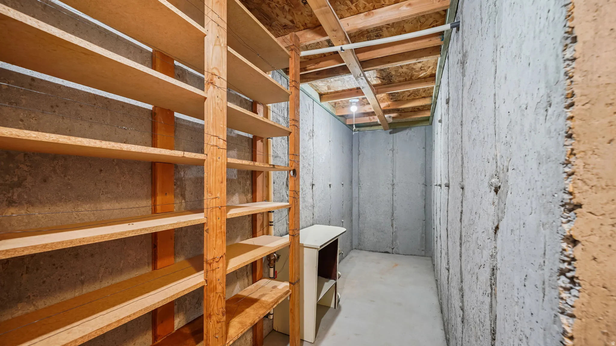 Extensive built-in shelving units in a storage room with concrete walls and an exposed wood ceiling