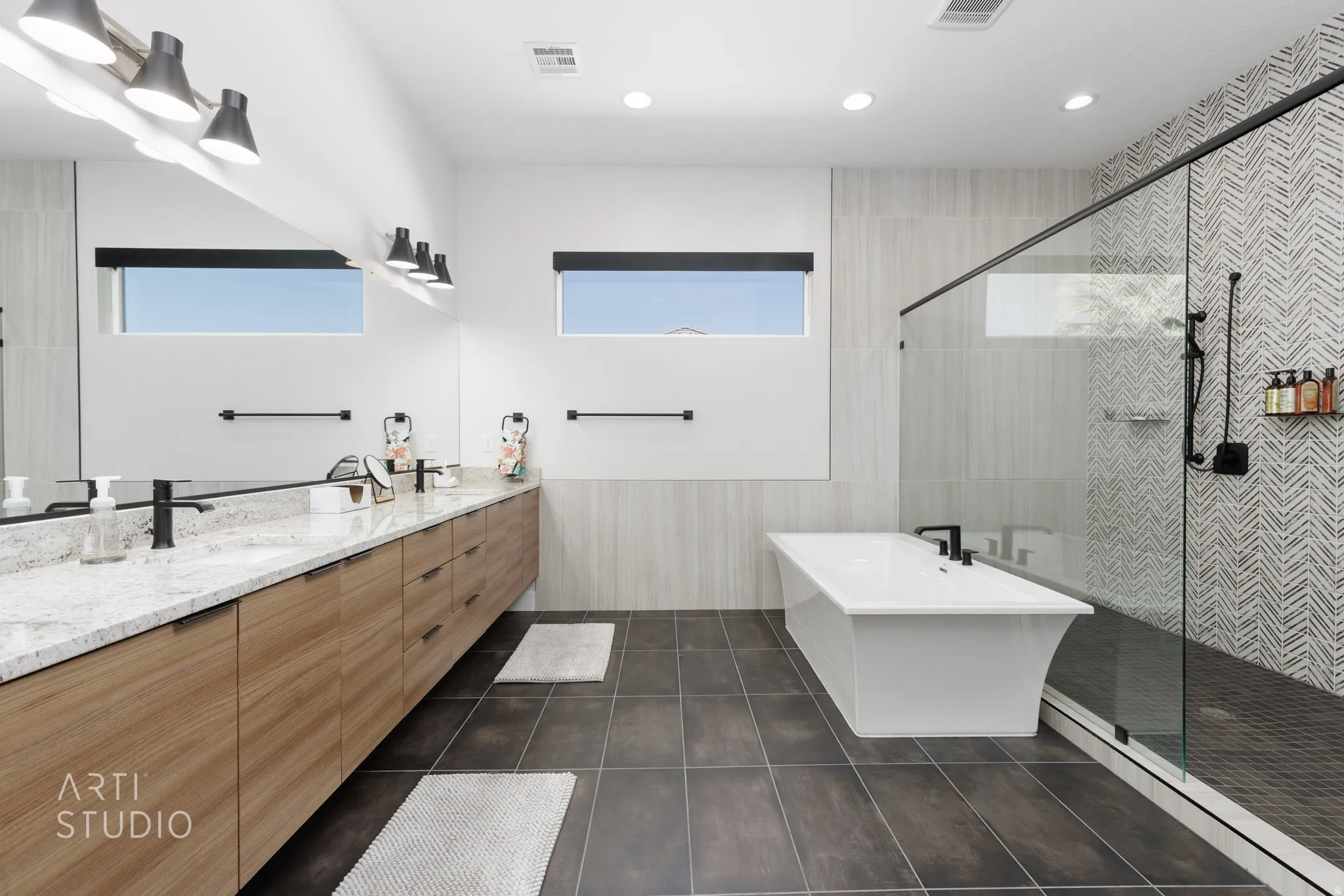 Contemporary bathroom featuring a freestanding soaking tub, a frameless glass-enclosed shower with herringbone tile, a double vanity with stone countertops, and wood-finish cabinetry