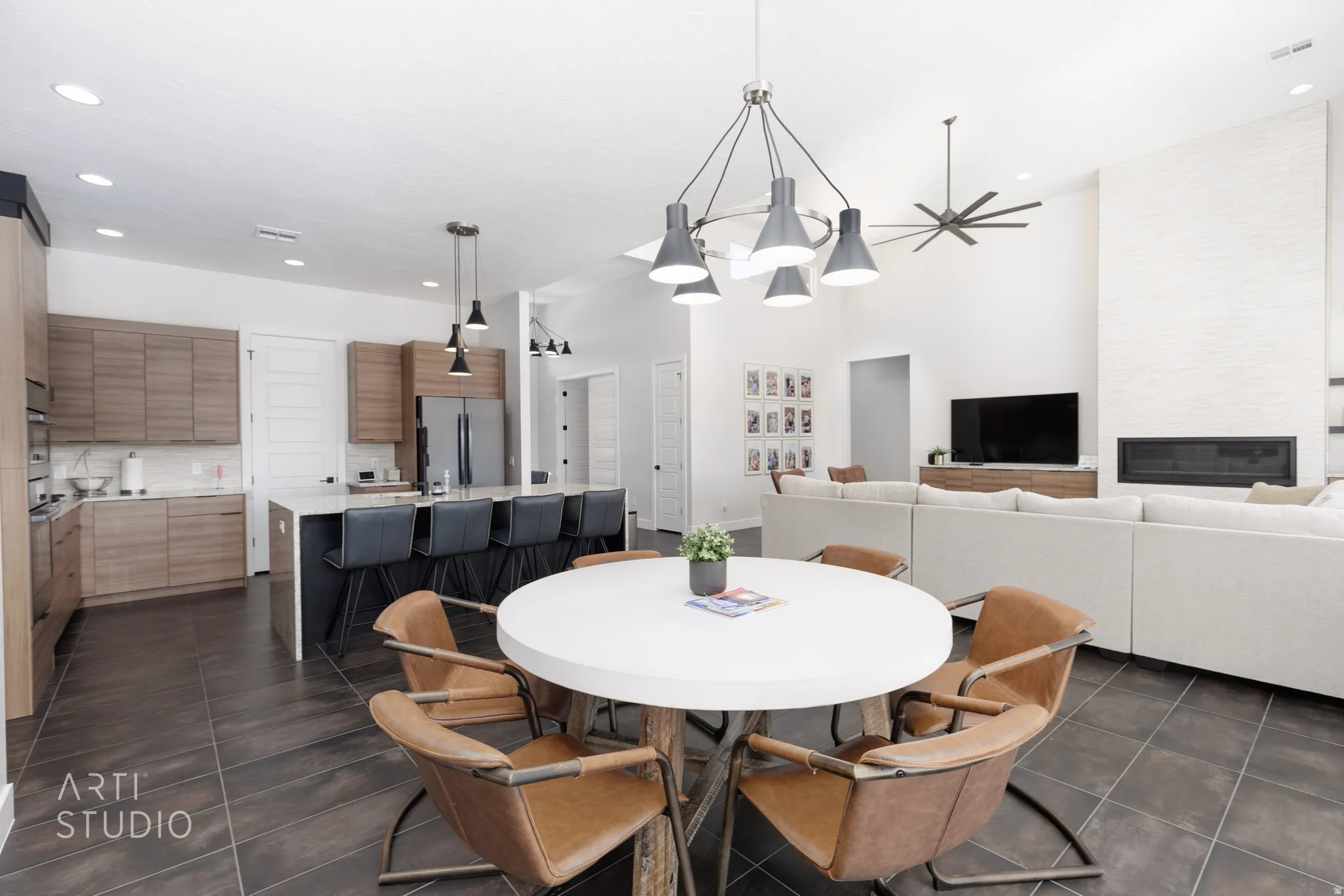 Open concept living area featuring wood-finish flooring, a contemporary kitchen with a large island and pendant lighting, a vaulted ceiling, and a linear fireplace within a textured white wall