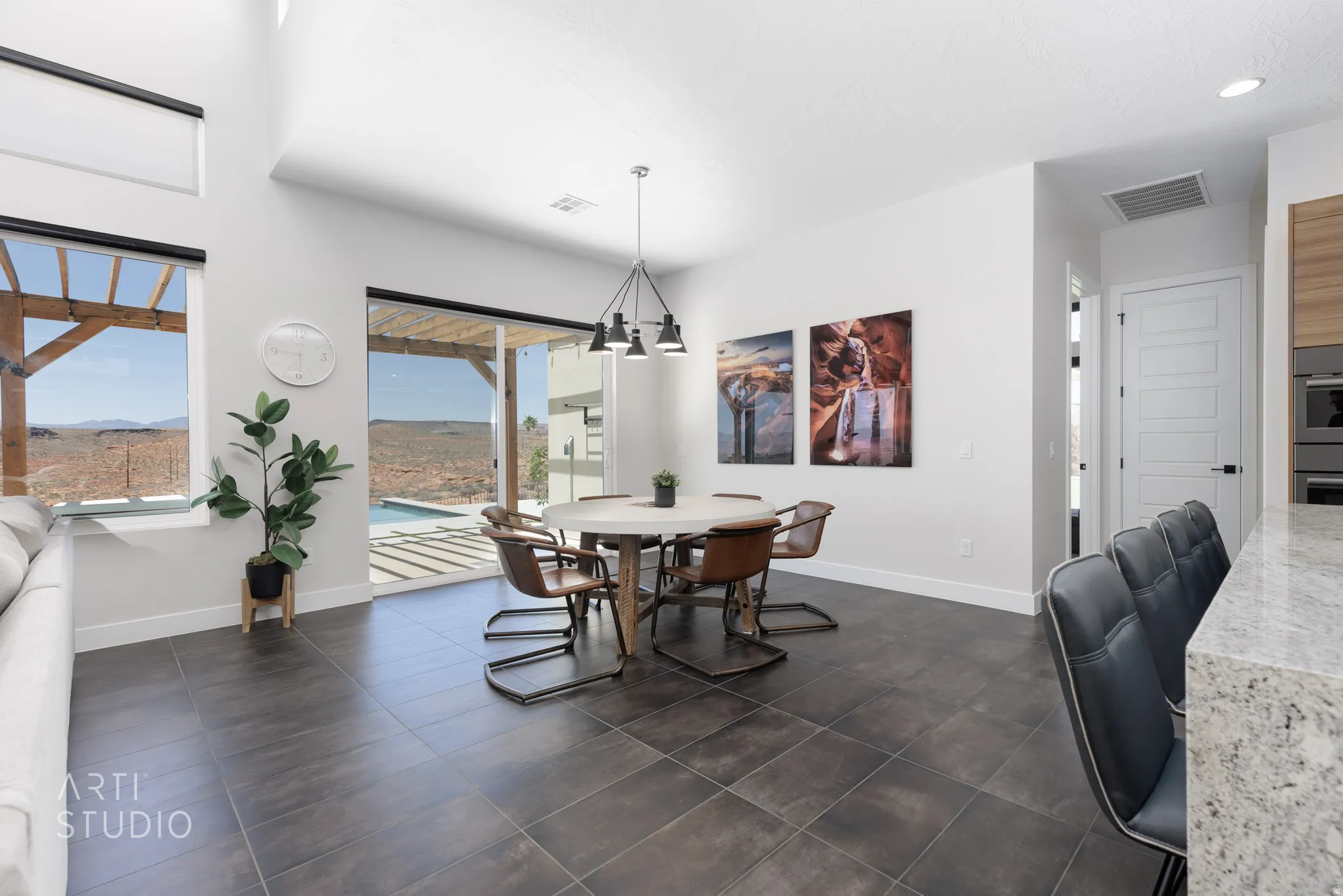 Open-concept dining area featuring dark tile flooring, a modern chandelier, and a sliding glass door leading to an outdoor living space with a pergola and pool