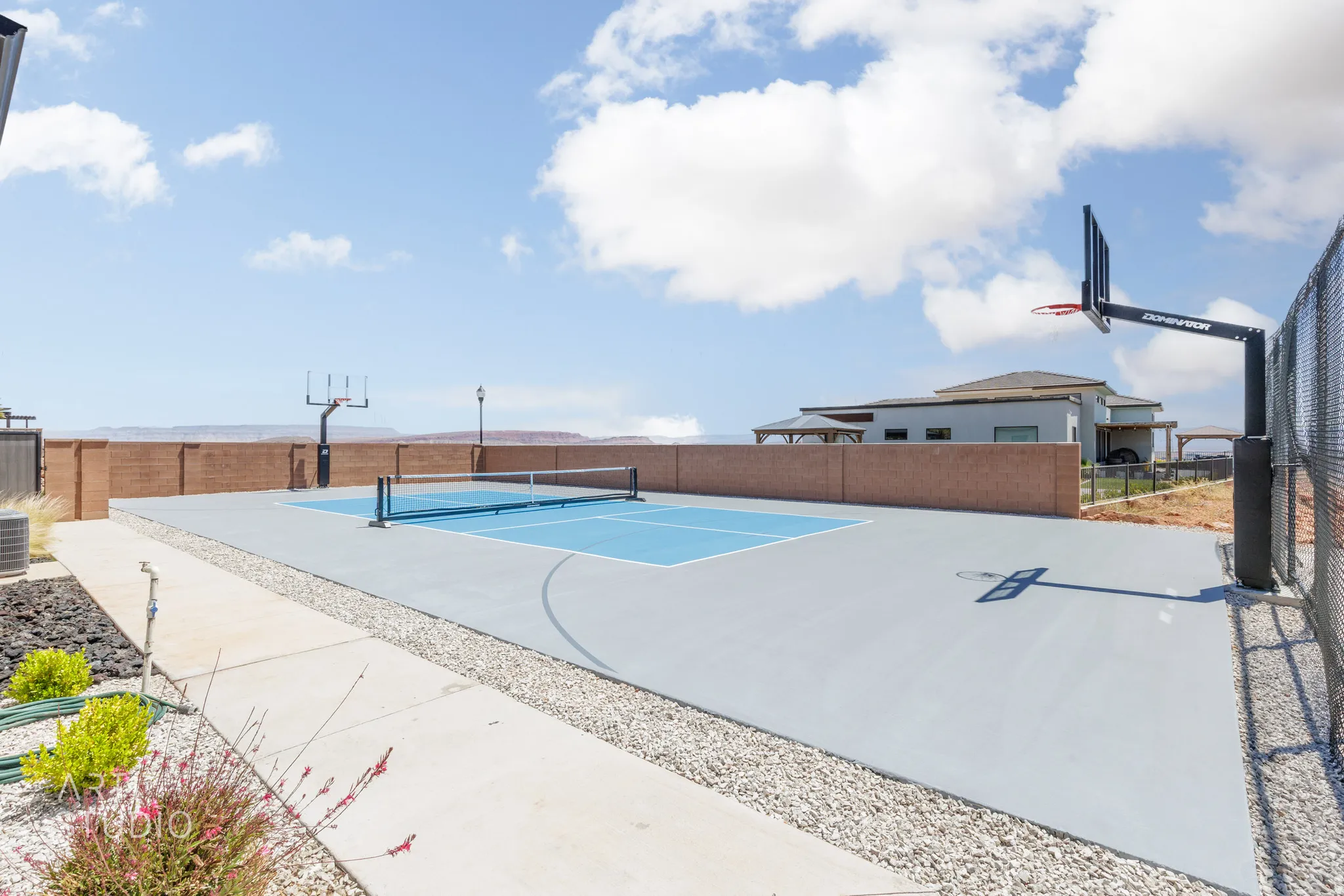 Multi-sport court featuring a painted blue pickleball surface and two basketball hoops