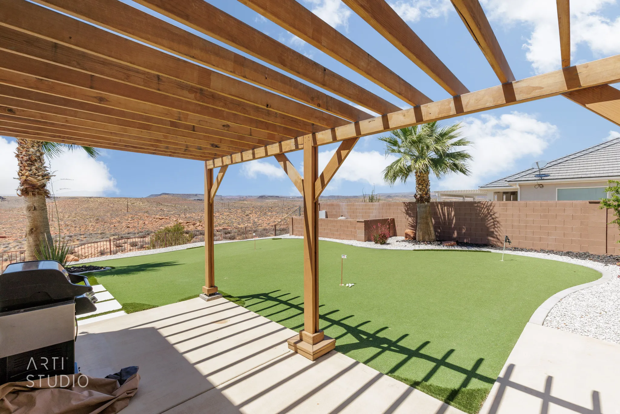 Expansive patio area featuring a wooden pergola, concrete flooring, and a putting green