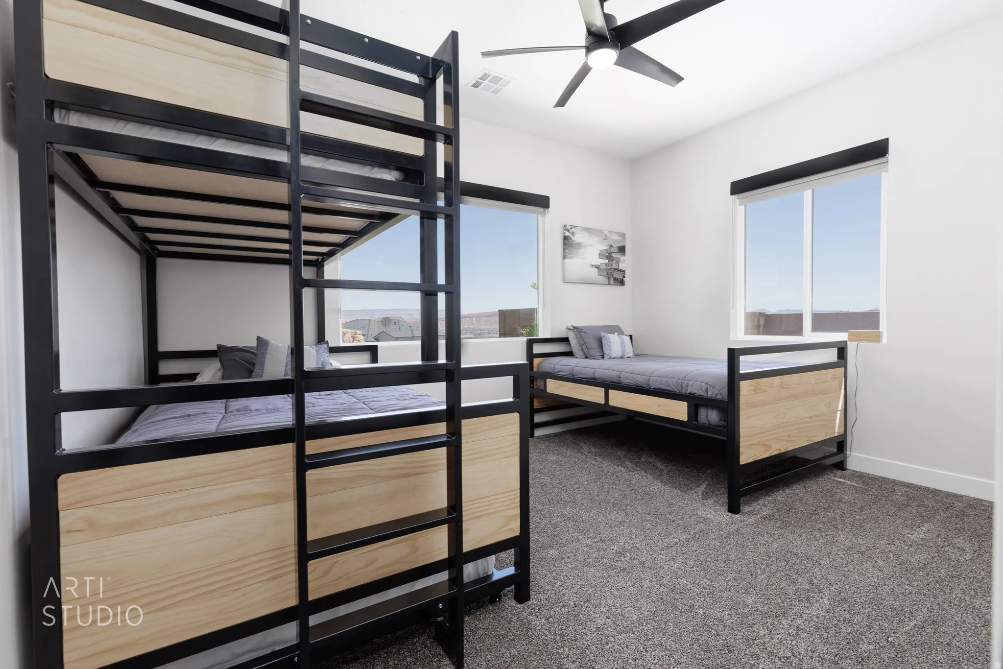 Bright interior space featuring a ceiling fan, two windows with roller shades, and grey carpet flooring