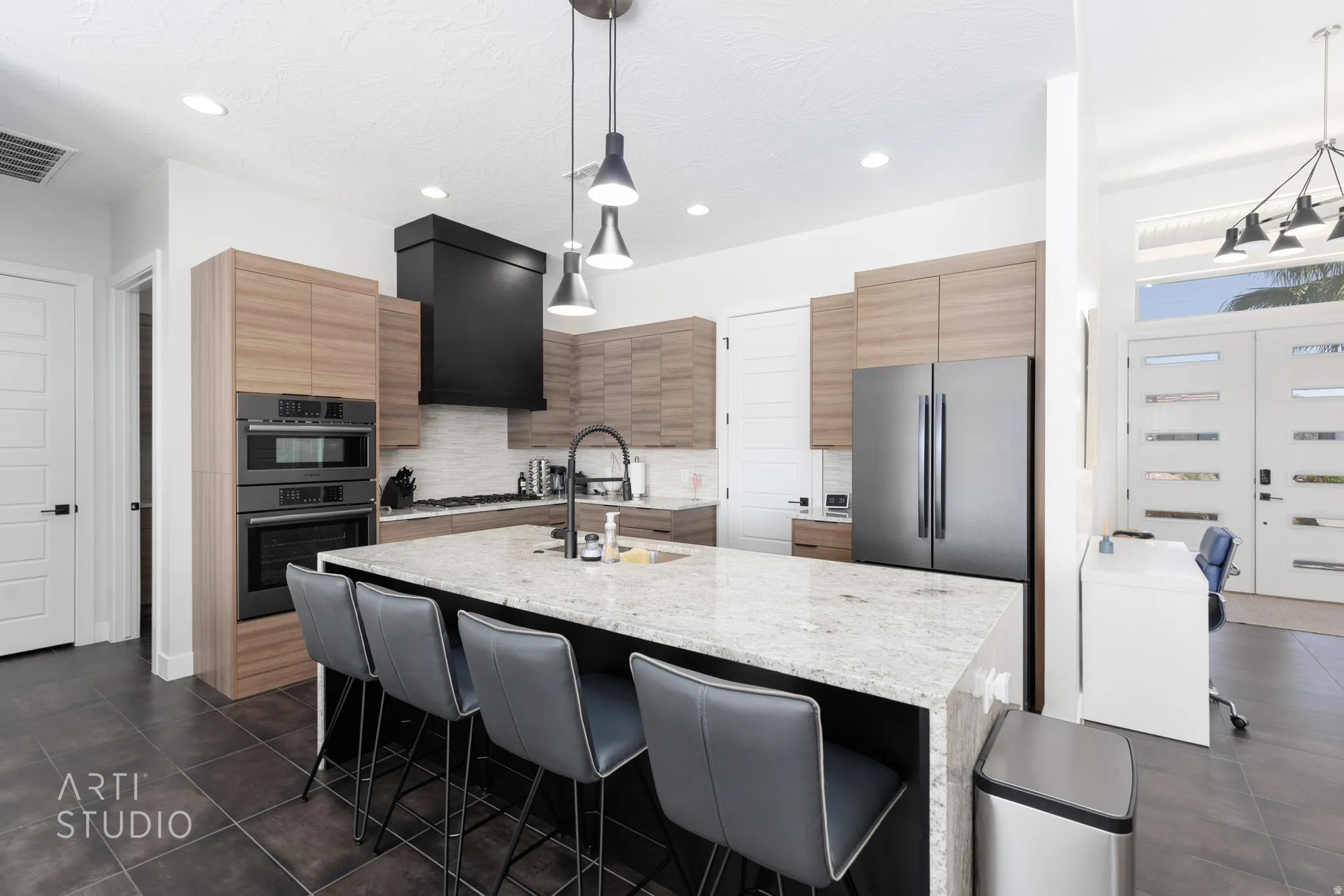Modern kitchen featuring a large island with seating, integrated appliances, wood-finish cabinetry, a black range hood, and pendant lighting