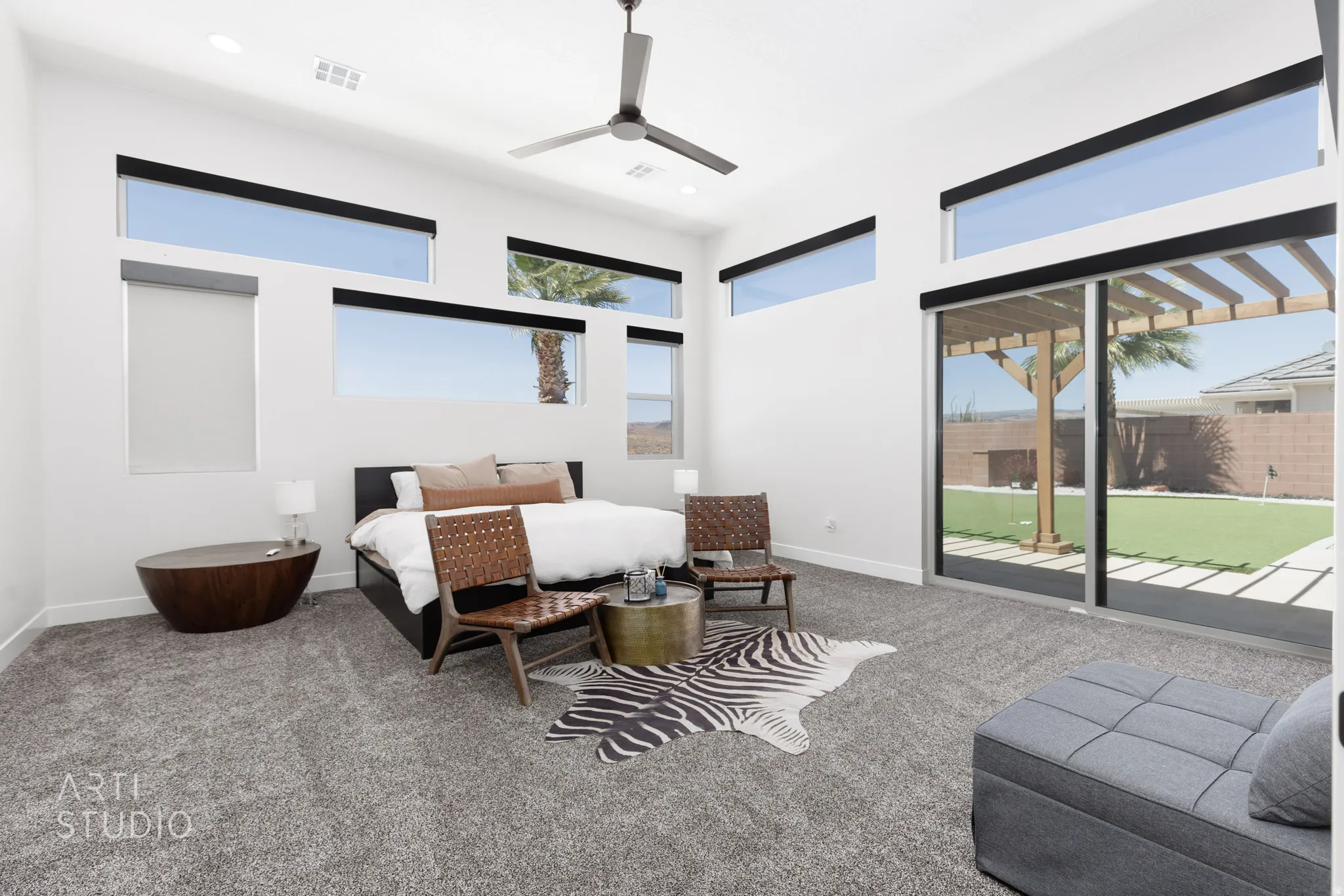 Vaulted ceiling with a contemporary ceiling fan, numerous clerestory windows with roller shades, and a sliding glass door leading to a backyard with artificial turf and a wooden pergola