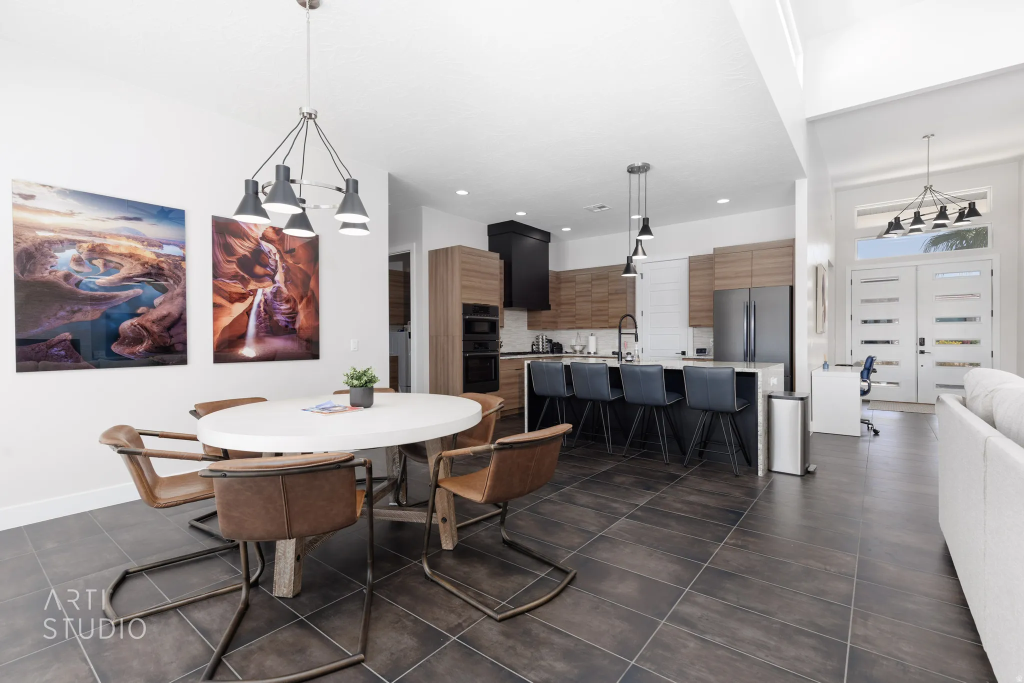Spacious open-concept living area featuring dark tile flooring, a modern kitchen with a large island, stainless steel appliances, and wood-finish cabinetry