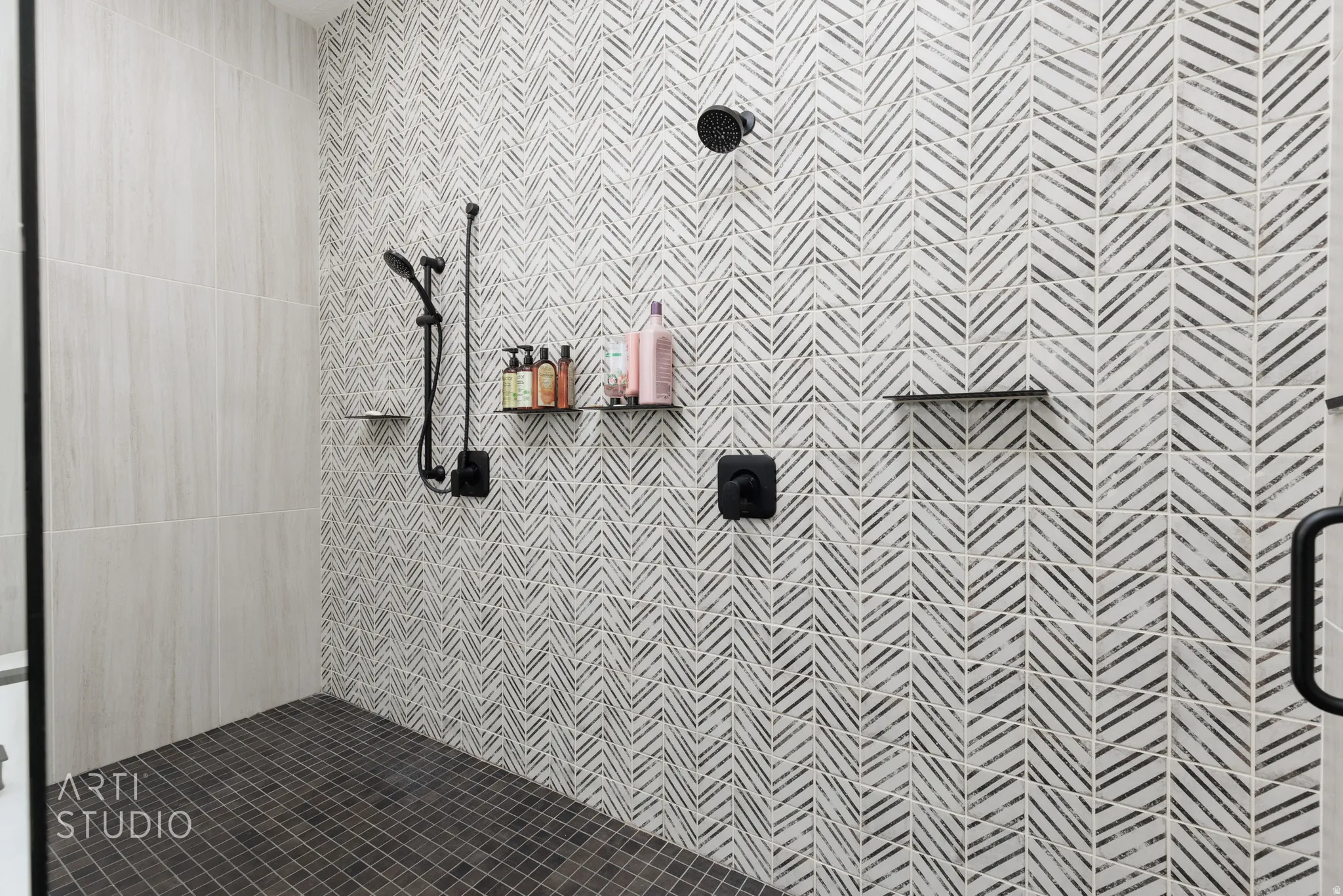 Walk-in shower featuring a chevron-patterned accent wall, matte black fixtures, integrated shower head, and a handheld shower wand