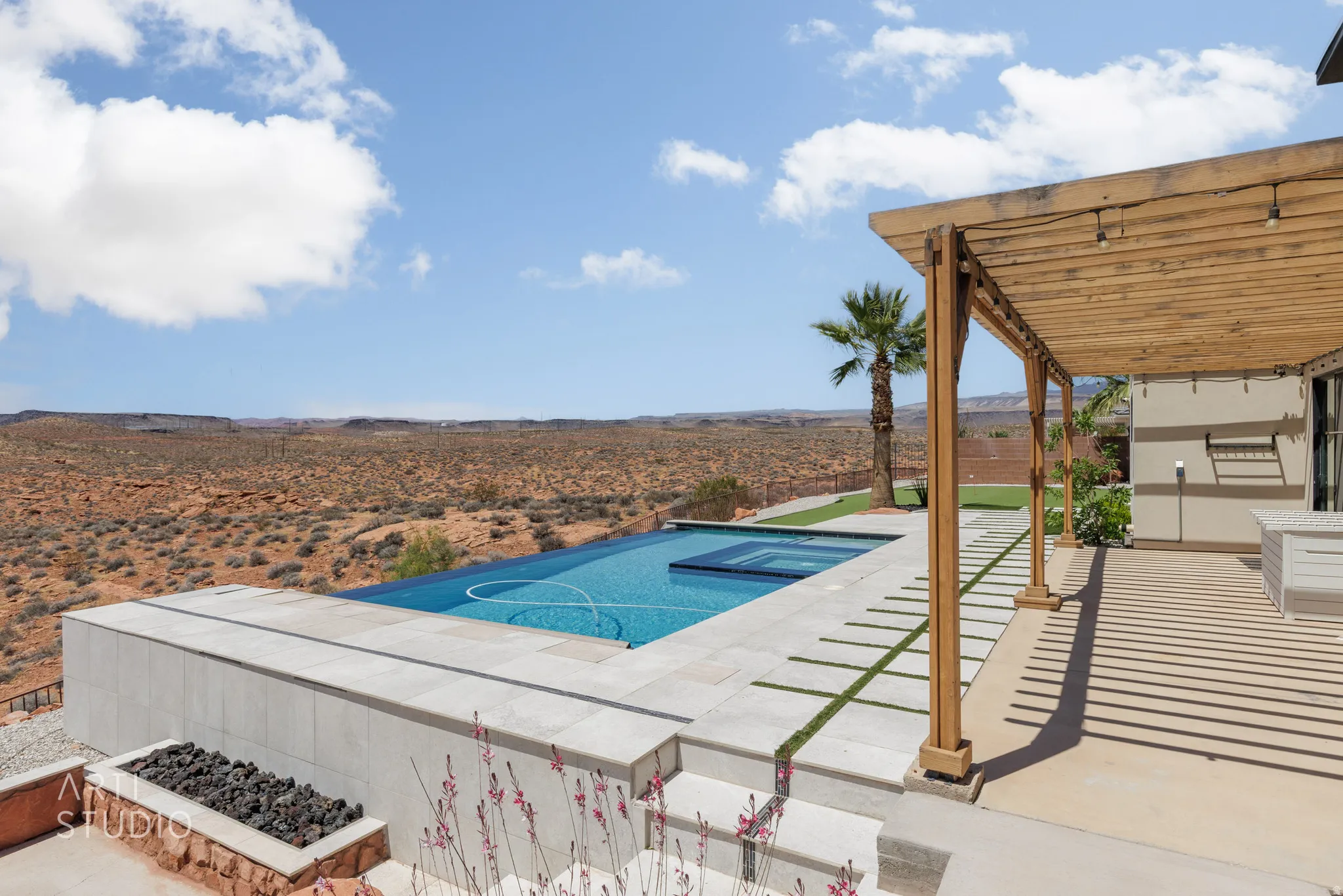 Expansive outdoor living area featuring a rectangular pool with an integrated spa, a wooden pergola, and a built-in fire pit with dark rock
