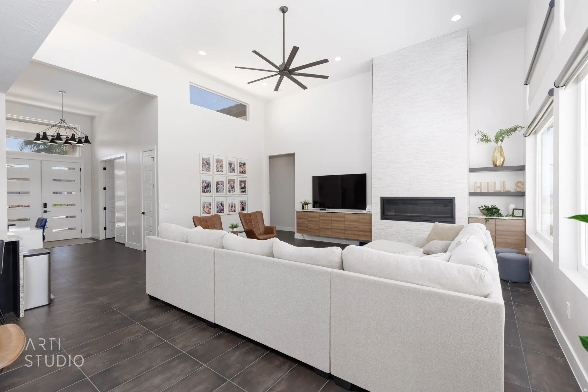 Vaulted ceilings with a prominent ceiling fan, large format tile flooring, a linear fireplace set within a textured white hearth, and abundant natural light from multiple windows