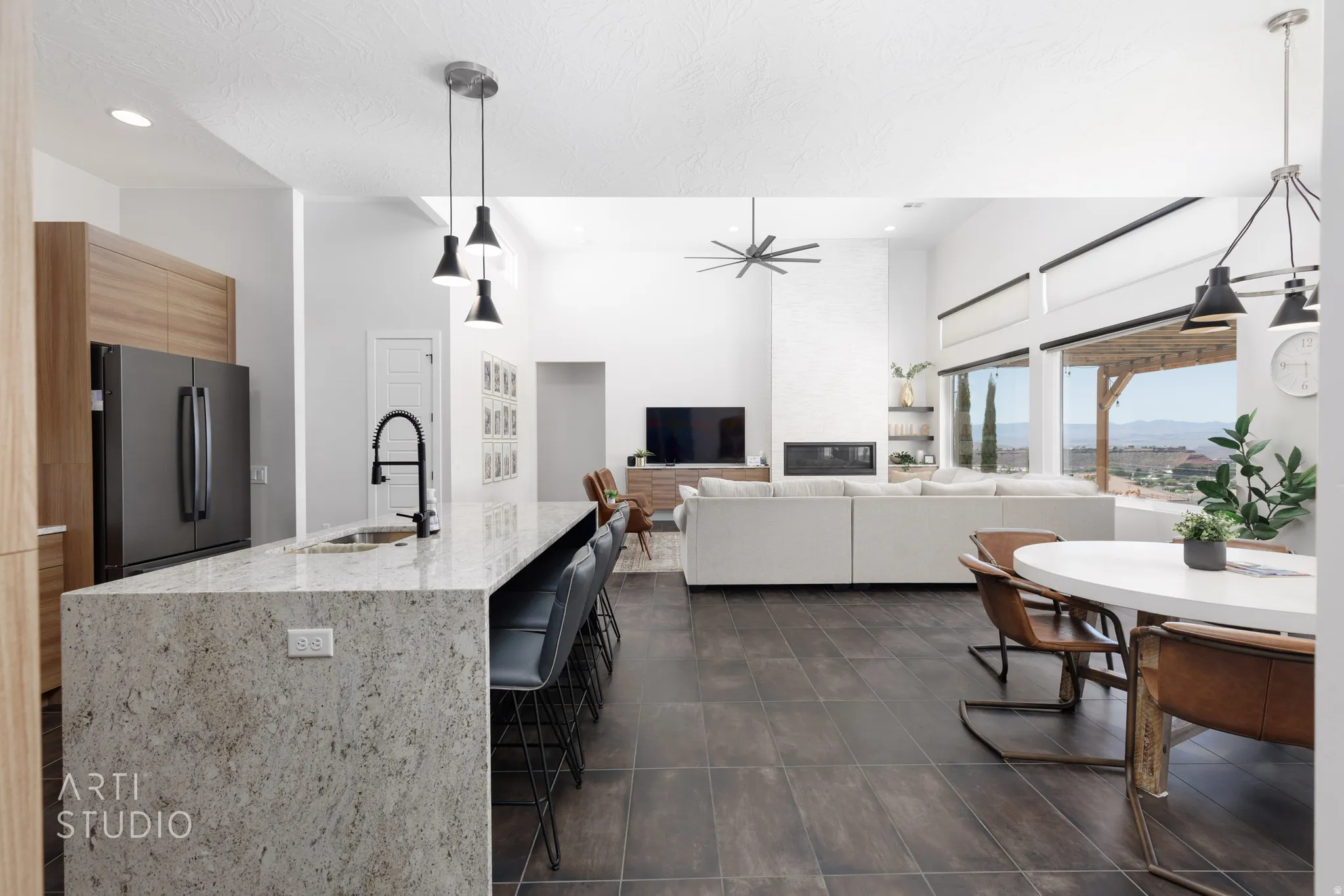 Open-concept living space featuring a large kitchen island with pendant lighting, dark tile flooring, a built-in fireplace, and expansive windows