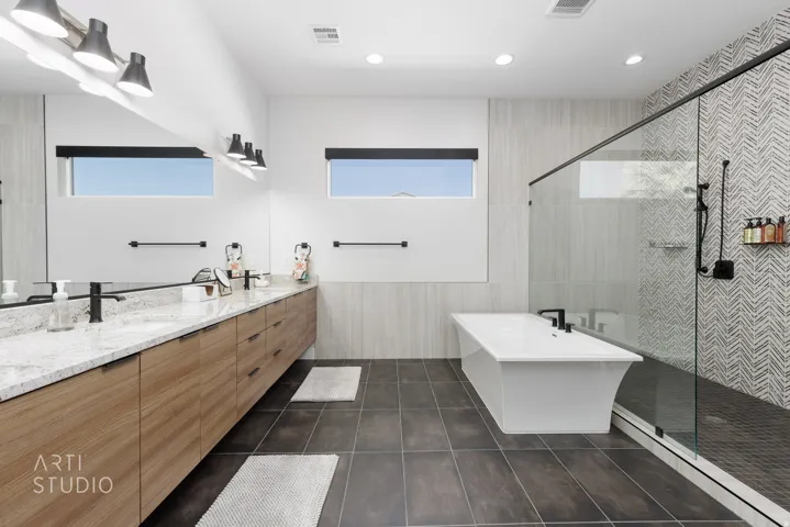 Contemporary bathroom featuring a freestanding soaking tub, a frameless glass-enclosed shower with herringbone tile, a double vanity with stone countertops, and wood-finish cabinetry
