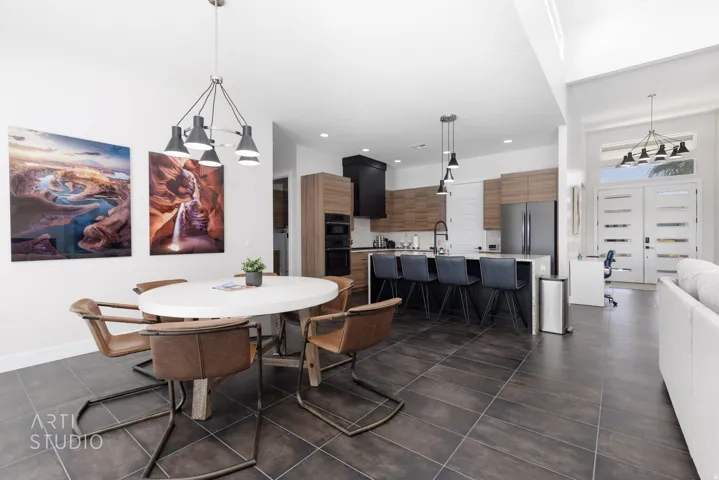Spacious open-concept living area featuring dark tile flooring, a modern kitchen with a large island, stainless steel appliances, and wood-finish cabinetry