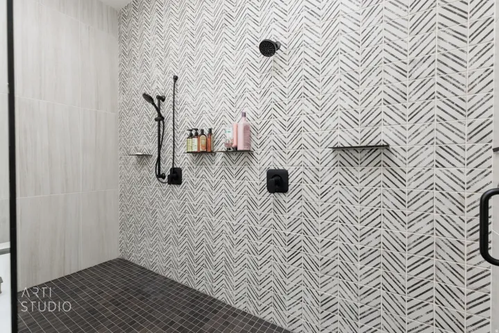 Walk-in shower featuring a chevron-patterned accent wall, matte black fixtures, integrated shower head, and a handheld shower wand