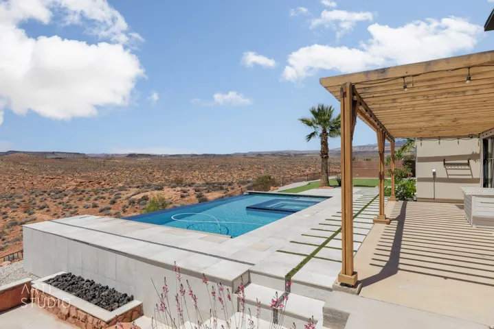 Expansive outdoor living area featuring a rectangular pool with an integrated spa, a wooden pergola, and a built-in fire pit with dark rock