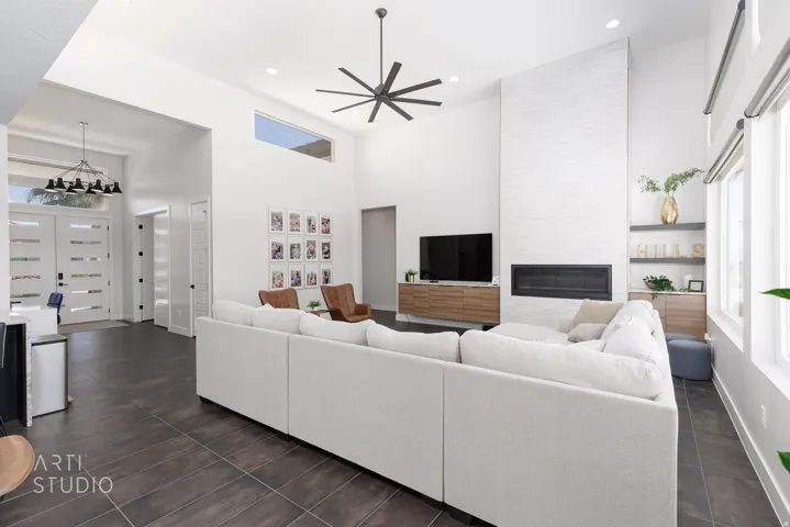 Vaulted ceilings with a prominent ceiling fan, large format tile flooring, a linear fireplace set within a textured white hearth, and abundant natural light from multiple windows