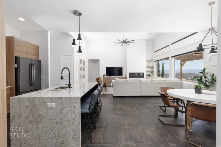 Open-concept living space featuring a large kitchen island with pendant lighting, dark tile flooring, a built-in fireplace, and expansive windows